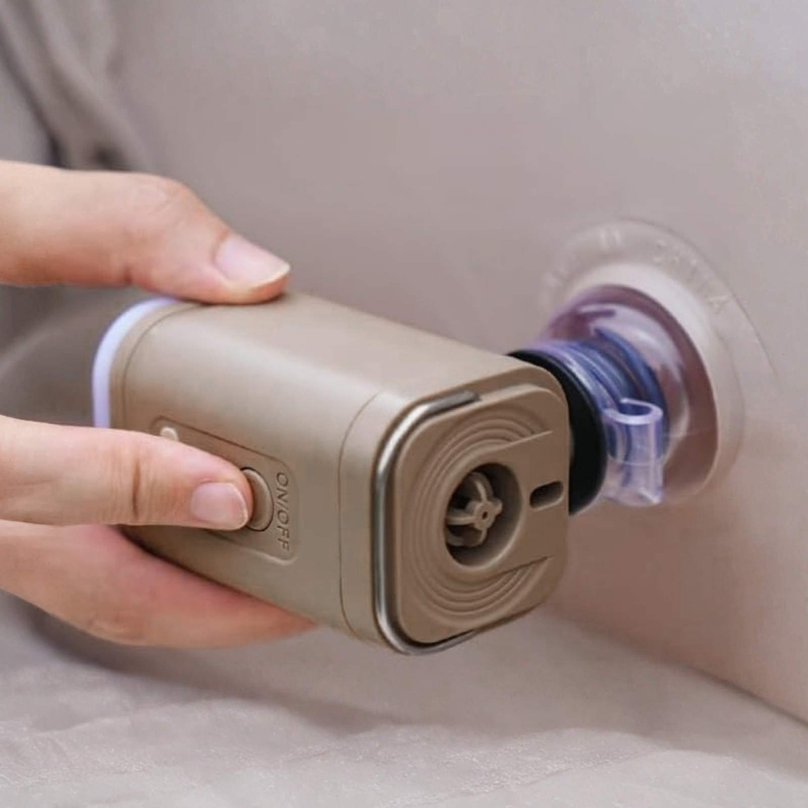 Eine Hand hält eine beige elektrische Pumpe, die mit einer klaren Kunststoffdüse an einem aufblasbaren Gegenstand befestigt ist.