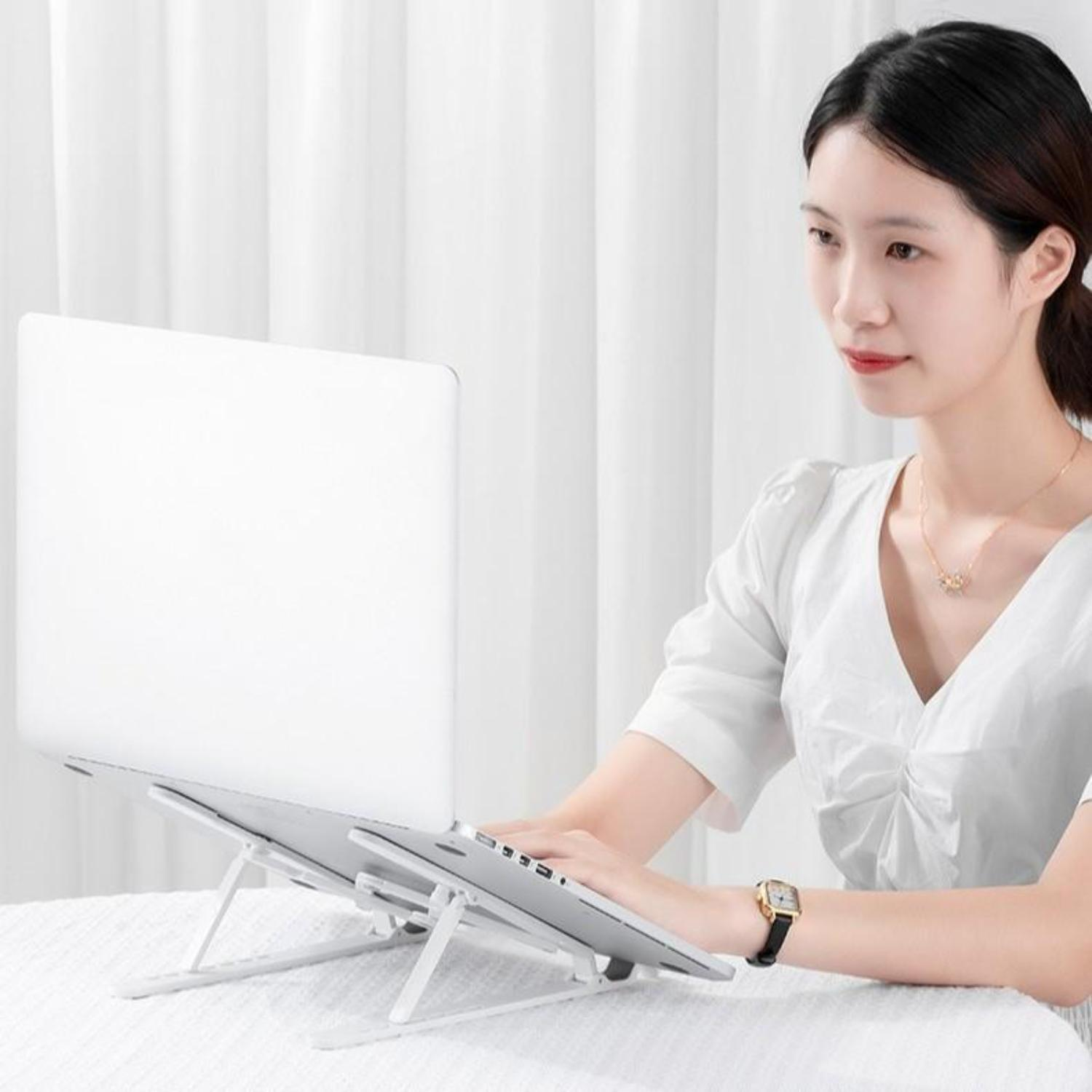 Frau benutzt einen Laptop auf einem weißen Laptop-Ständer. Heller Tisch und Wand im Hintergrund.