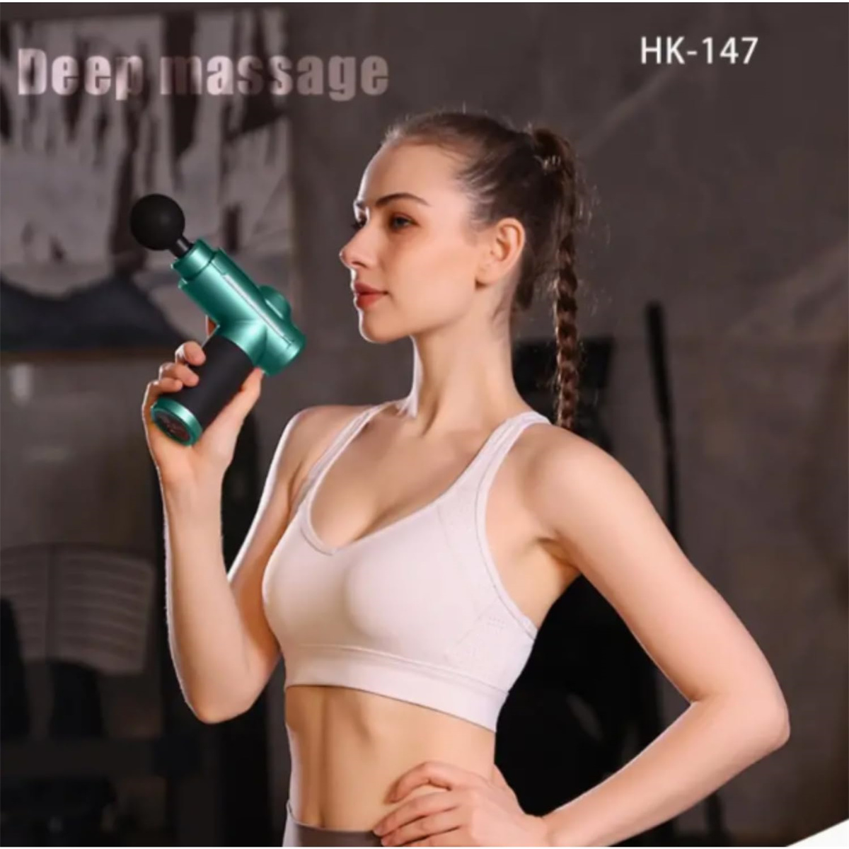 Eine Frau hält eine türkisfarbene Massagepistole. Sie trägt ein weißes Oberteil und steht in einem Raum mit Trainingsgeräten.