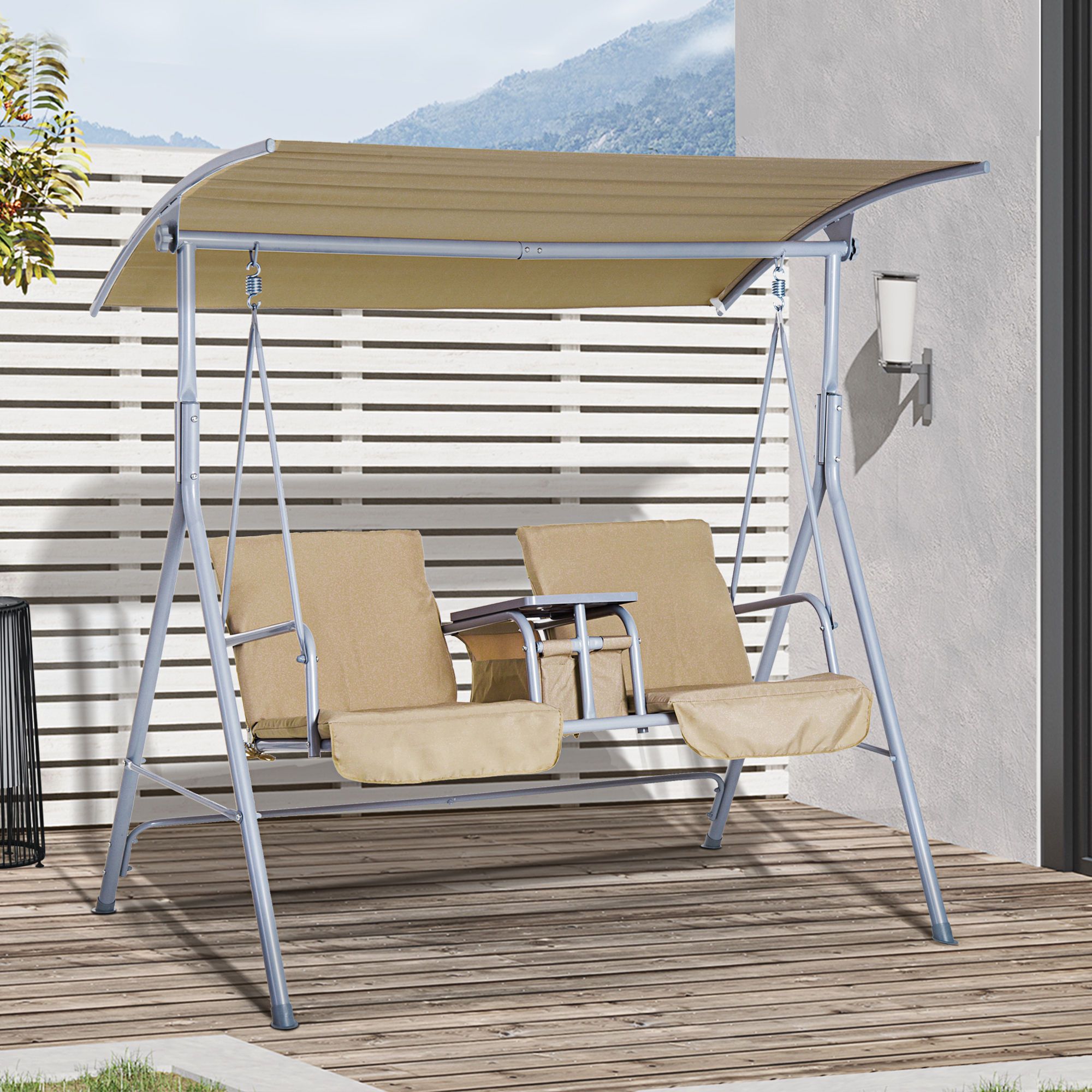 Ein beiges Schaukelset auf einer Holzterrasse. Die Schaukel hat ein Verdeck. Im Hintergrund ein Berg und Zaun.