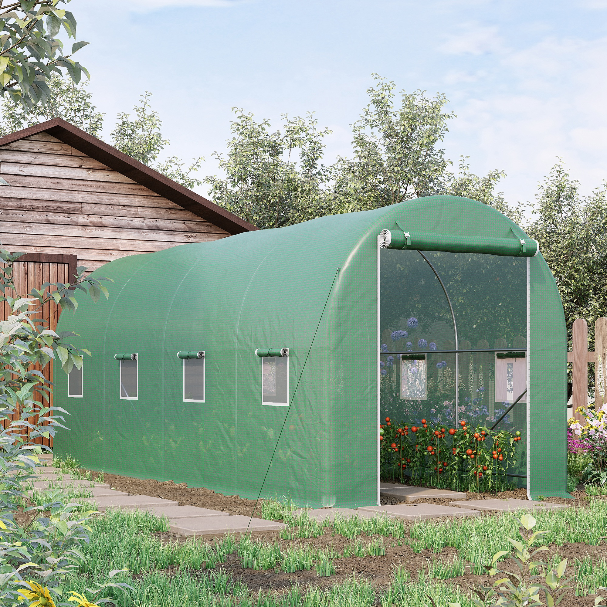 Un invernadero verde en un jardín. El invernadero está lleno de plantas. El contexto incluye una casa y árboles.
