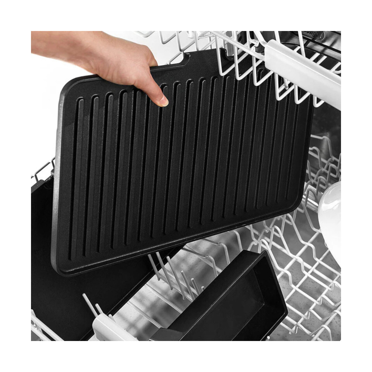 Ręka trzyma czarną płytę grillową. Płyta znajduje się w koszu zmywarki.