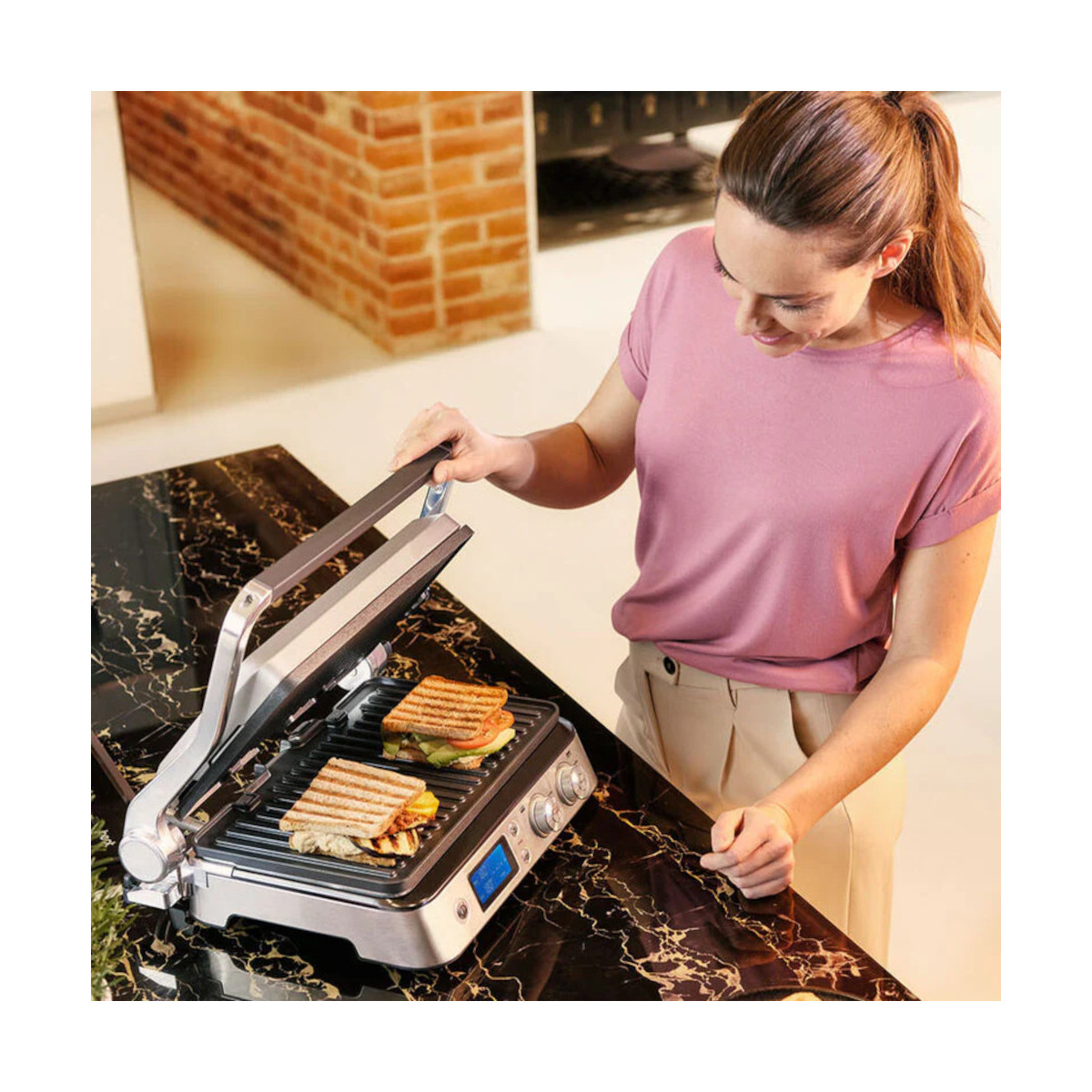 Kobieta używa grilla. Dwie kanapki są grillowane. Grill ma cyfrowy wyświetlacz.