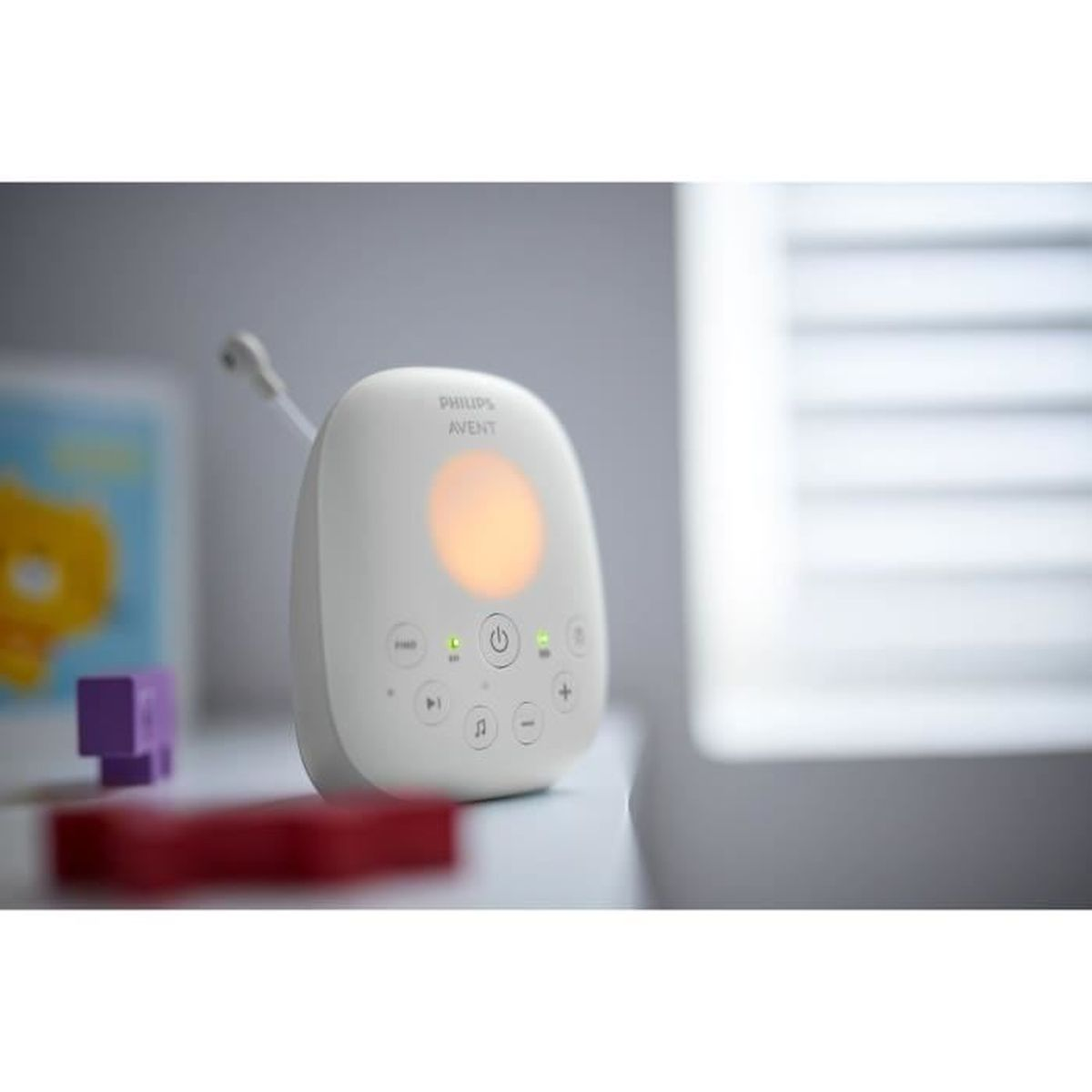 Ein weißer Baby-Monitor mit Knöpfen und einem kreisförmigen Licht. In der Nähe befinden sich ein roter und ein violetter Block.