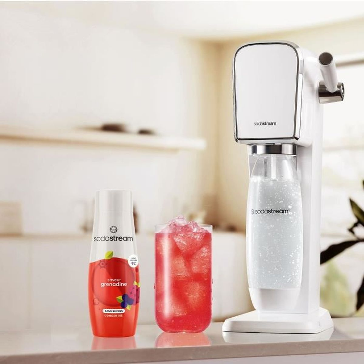 Eine SodaStream-Maschine, ein Glas rotes Getränk und eine Flasche Grenadine-Aromakonzentrat.