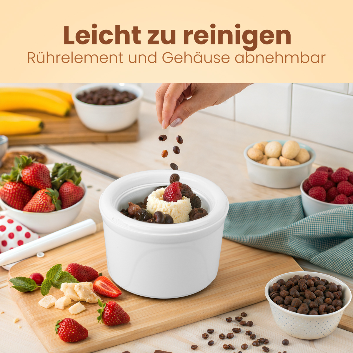 Ręka posypuje ziarna kawy lodami waniliowymi w białej misce. Truskawki, orzechy i inne składniki otaczają miskę na drewnianej desce.