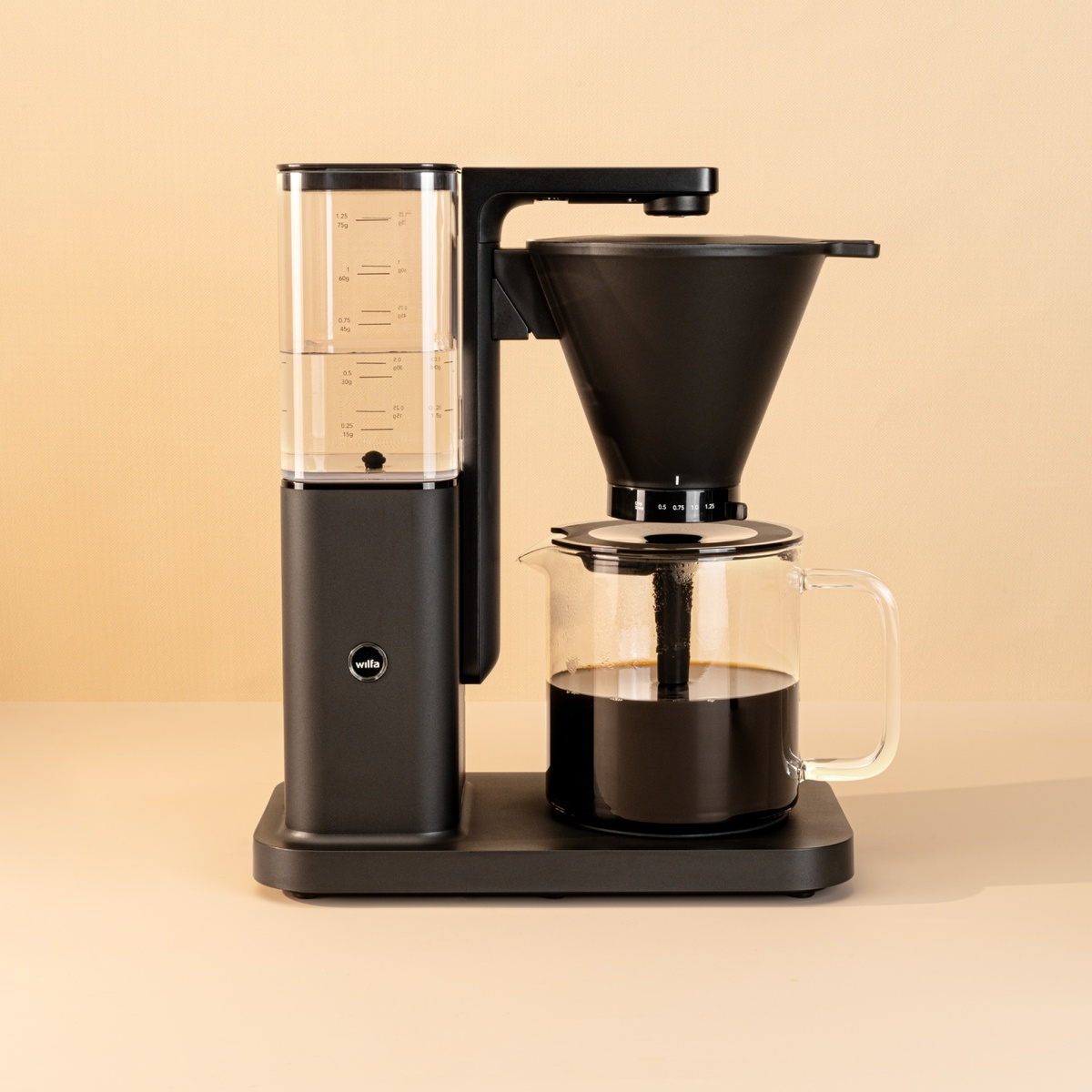 Macchina da caffè nera con serbatoio dell'acqua e caraffa in vetro. Si trova su una superficie beige.