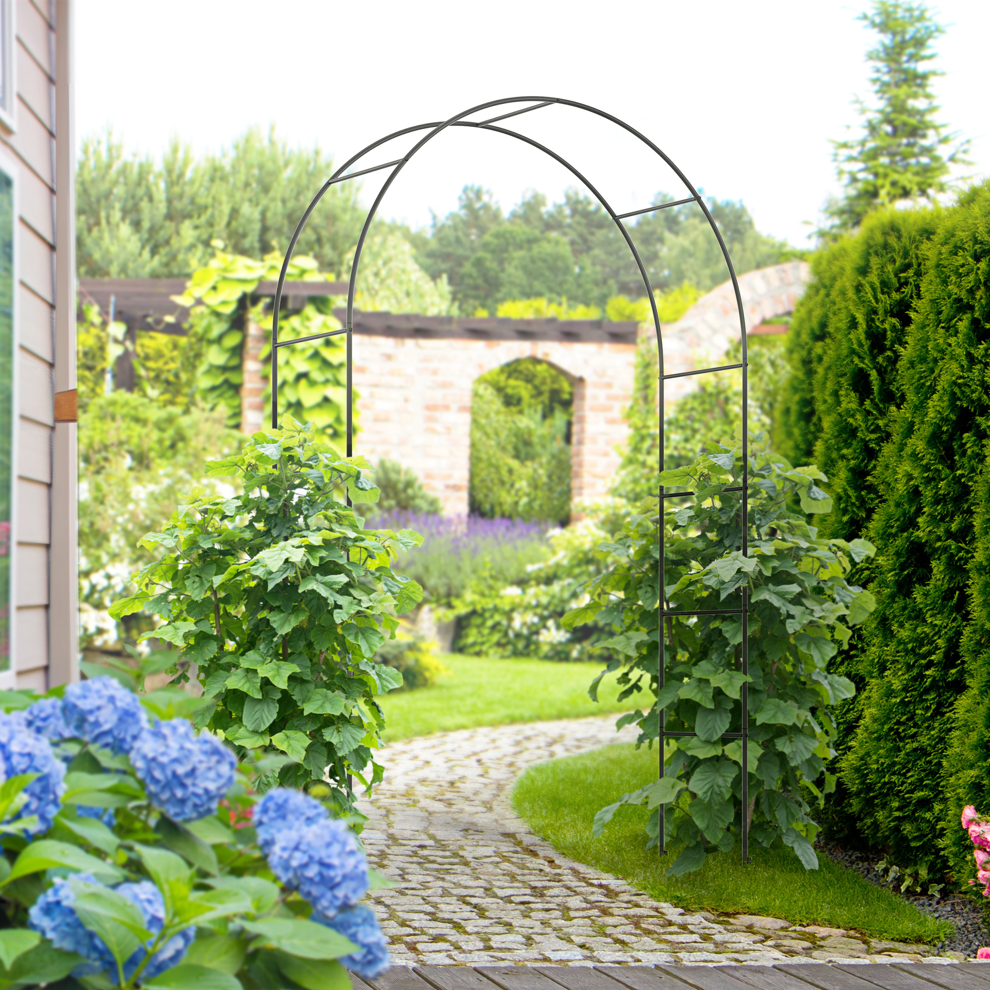 Ein Gartenbogen mit Kletterpflanzen steht auf einem Steinpfad, der zu einem Garten führt. Blaue Blumen im Vordergrund.
