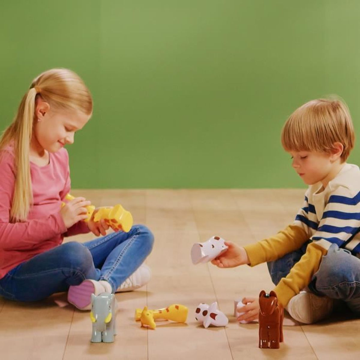 Due bambini giocano con pezzi di puzzle di animali. I bambini sono seduti davanti a un muro verde.