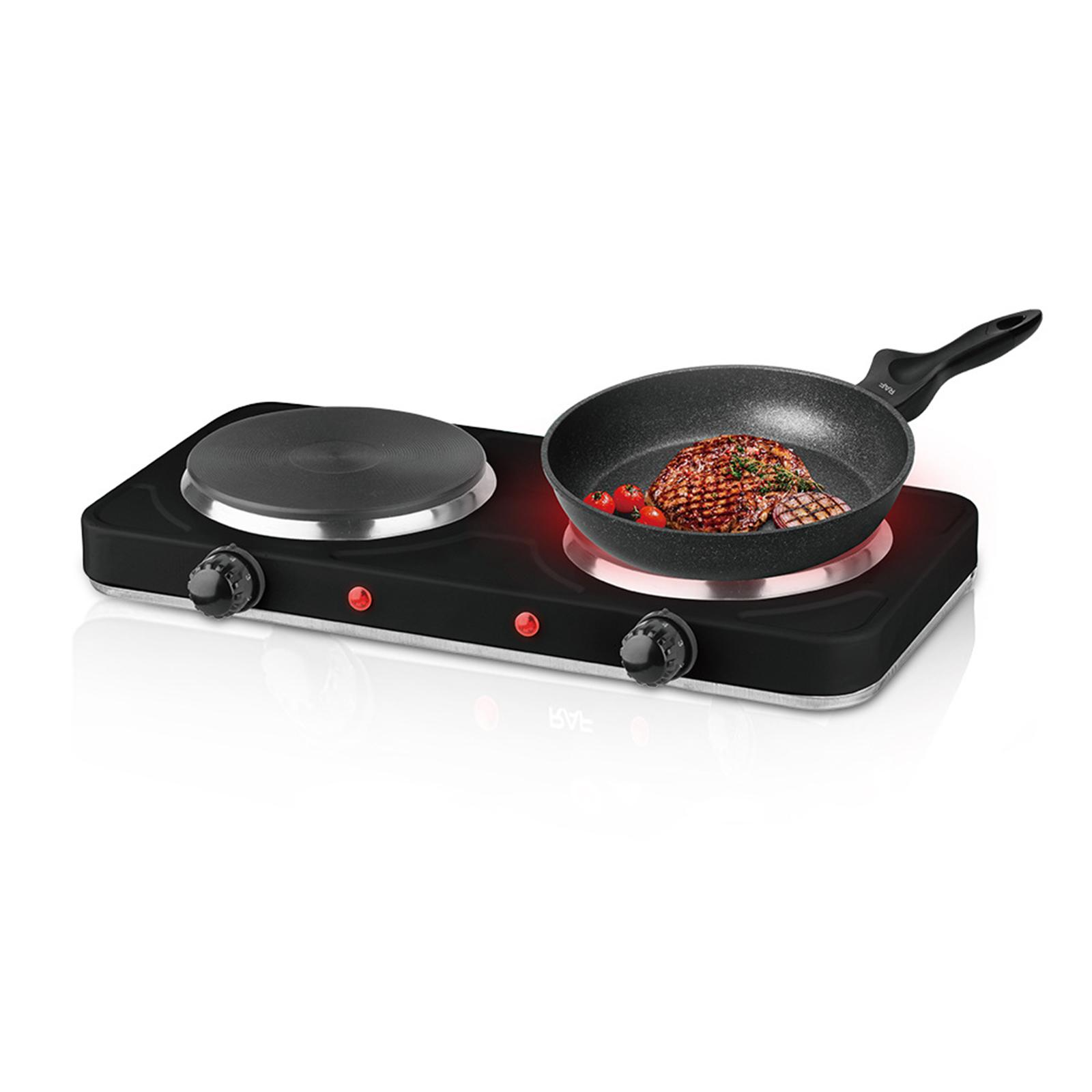 Ein schwarzer Elektroherd mit zwei Kochfeldern. Ein Steak und Tomaten werden in einer Pfanne auf einem Kochfeld gebraten. Rote Kontrollleuchten leuchten.