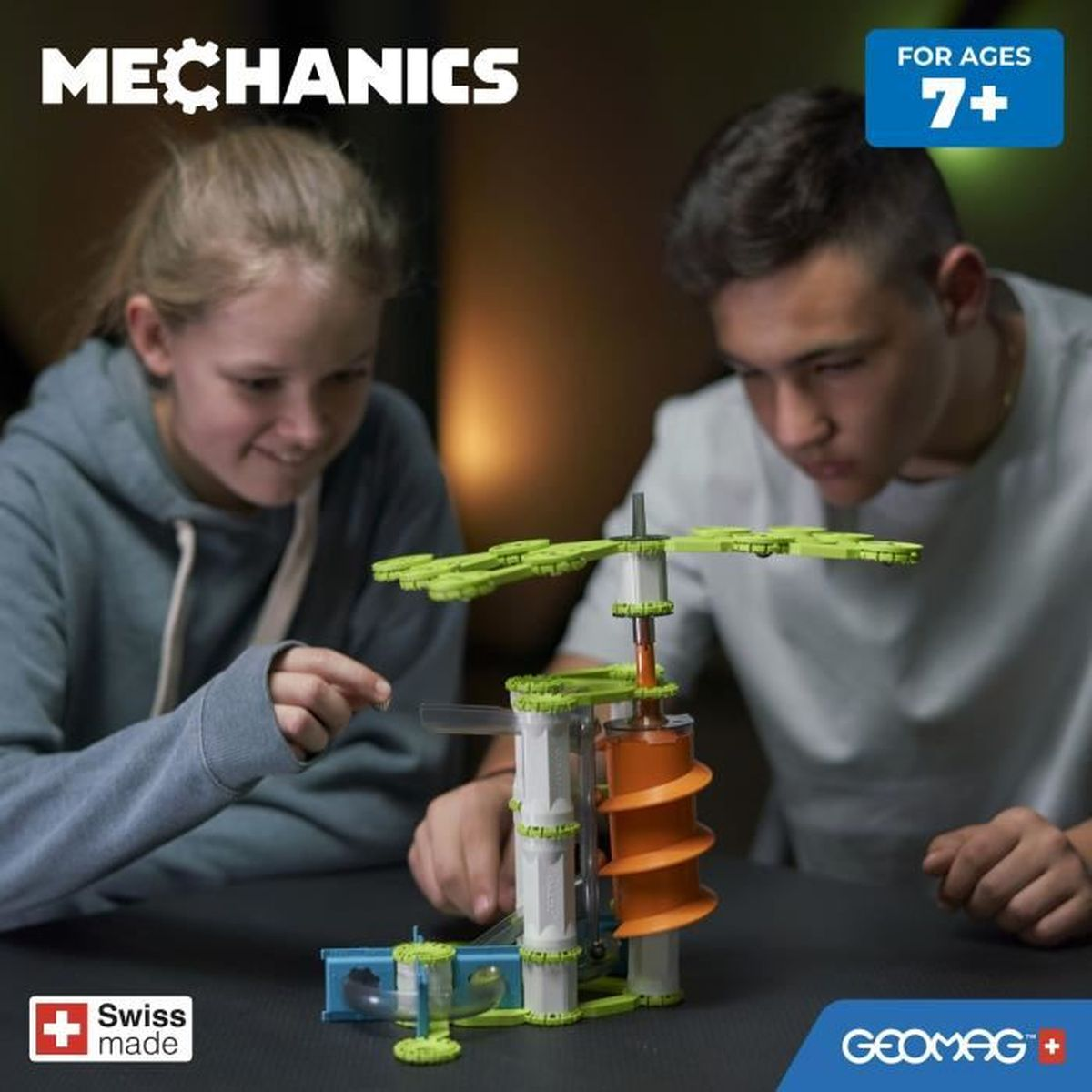 Due bambini che costruiscono un giocattolo STEM. Il giocattolo è verde, arancione e bianco con un logo Swiss made.