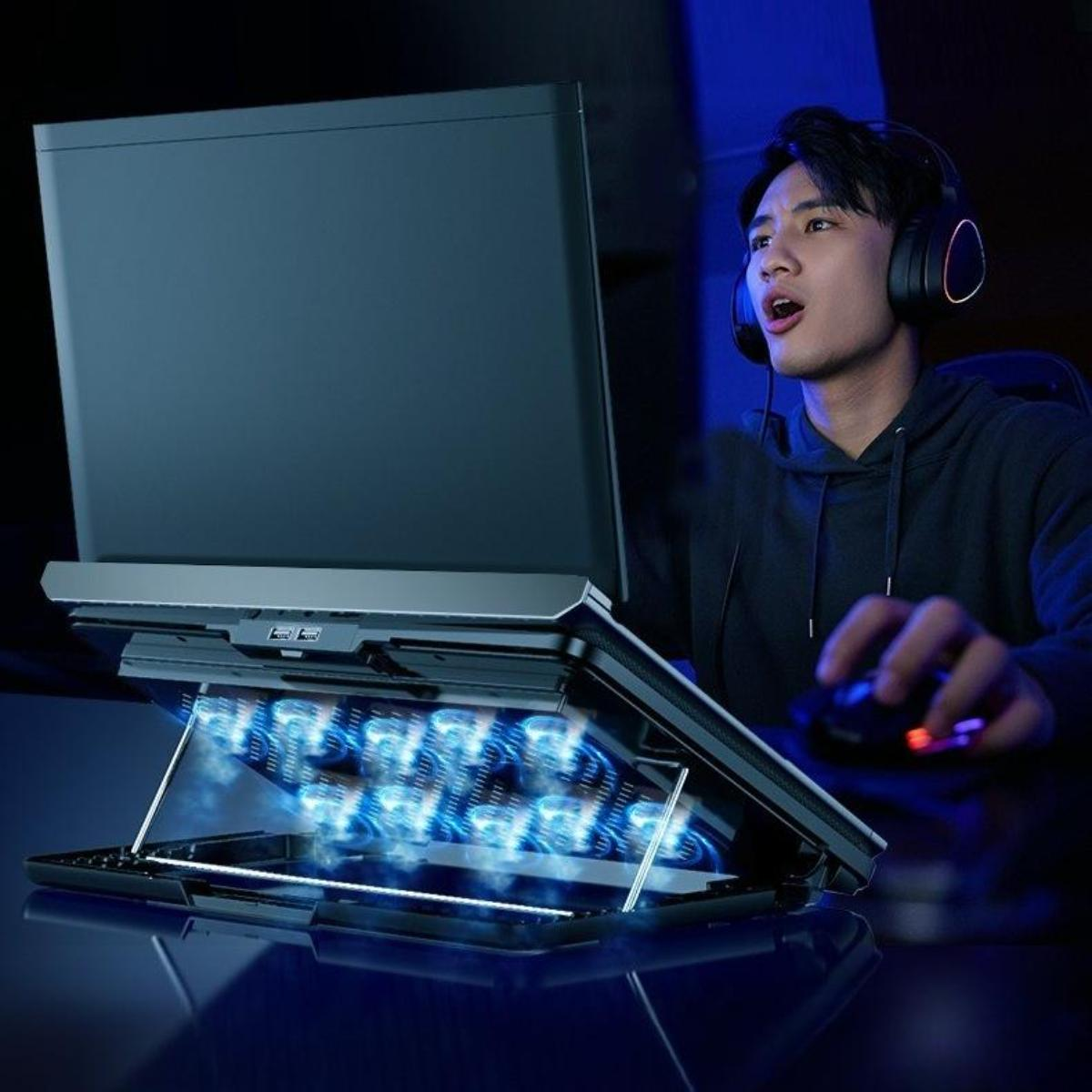 Ein Mann mit Kopfhörern spielt auf einem Laptop auf einem Kühlständer, mit blauen Lichteffekten.