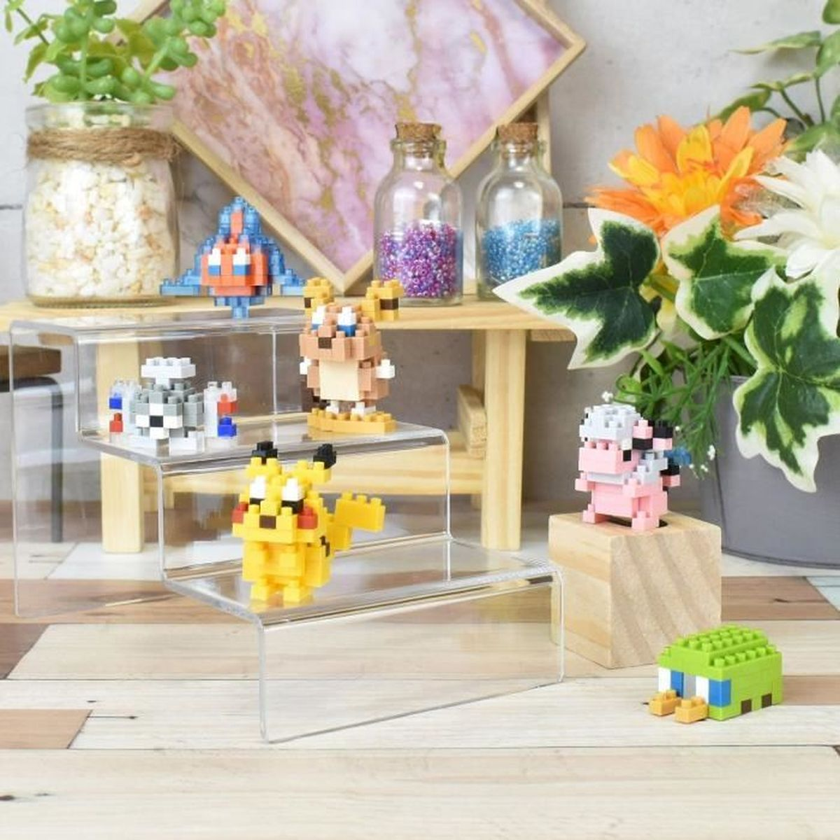 Mehrere Pokemon-Spielzeuge auf gestaffelten Stufen. Der Hintergrund hat ein Holzregal mit Gläsern und Blumen.