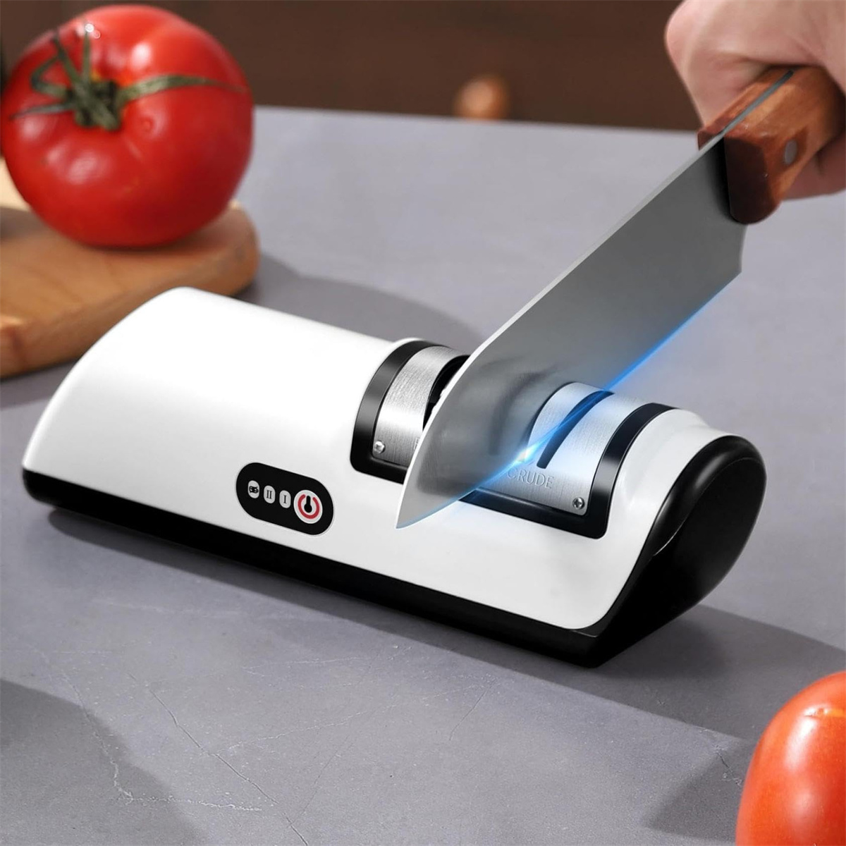 Eine Person, die ein Messer auf einem weiß-schwarzen Messerschärfer schärft, mit einer Tomate im Hintergrund.