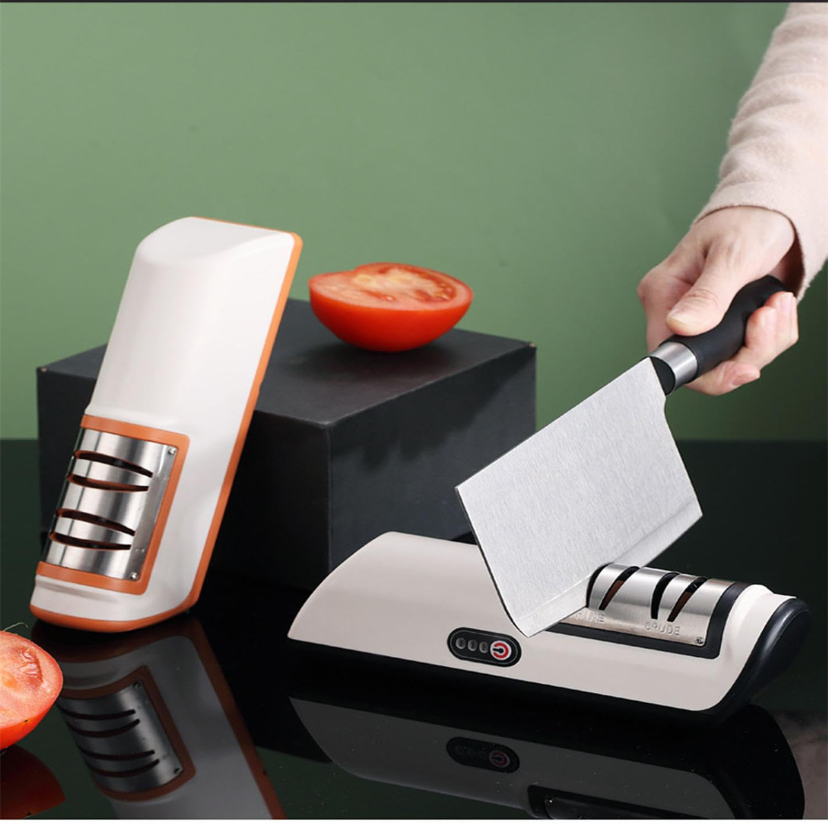 Ein Messerschärfer, Tomate und eine Hand, die ein Messer hält, auf glänzender schwarzer Oberfläche.