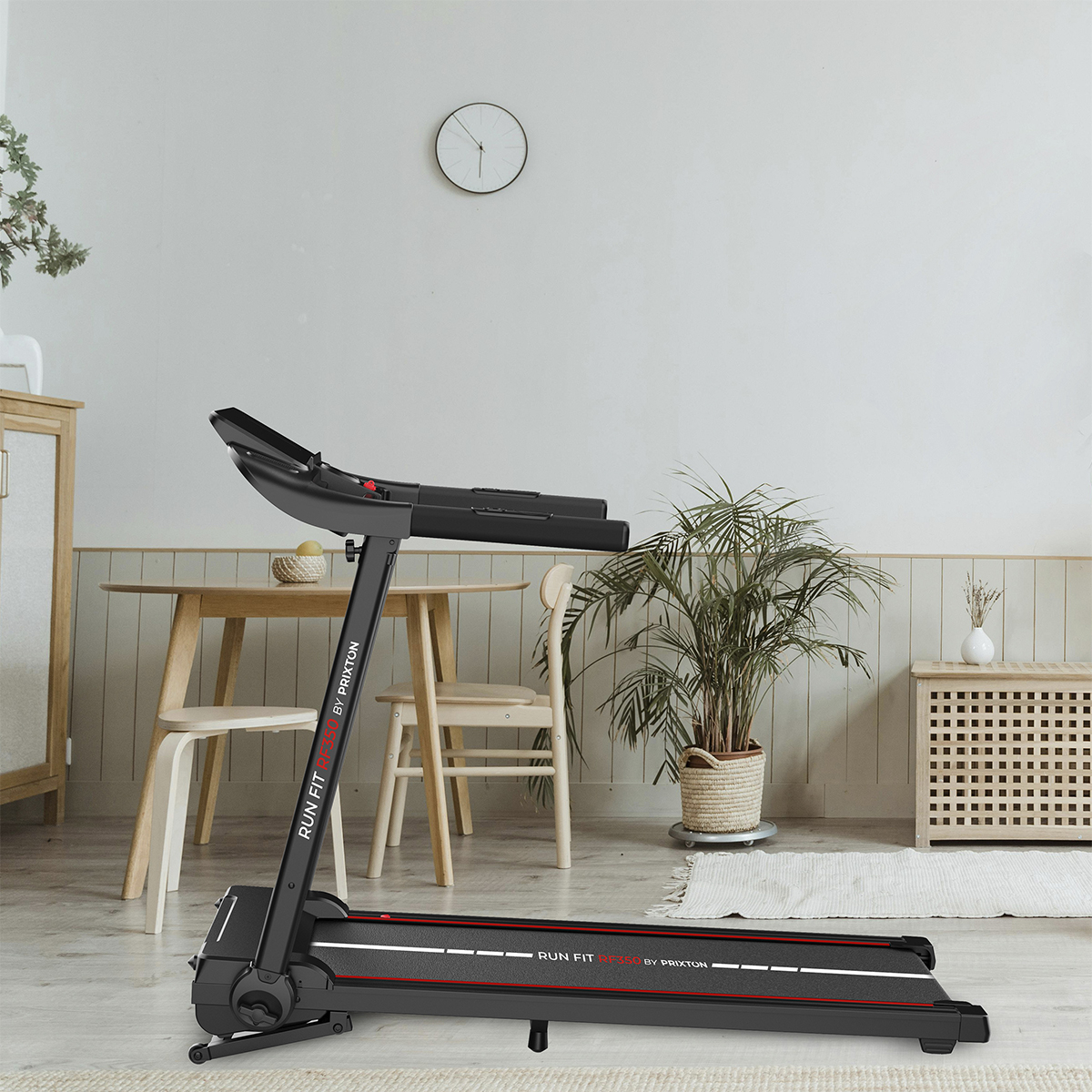 Czarna bieżnia w pokoju ze stołem, krzesłami i rośliną. Zegar wisi na ścianie.