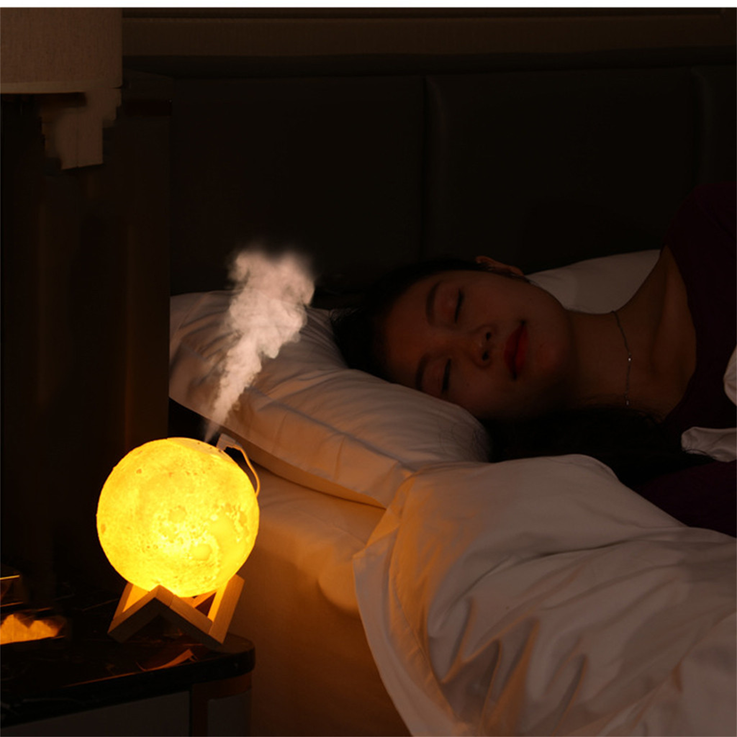 Eine Frau schläft im Bett mit einer mondförmigen Lampe. Dampf steigt von der Lampe auf. Weißes Kissen und Bettwäsche.