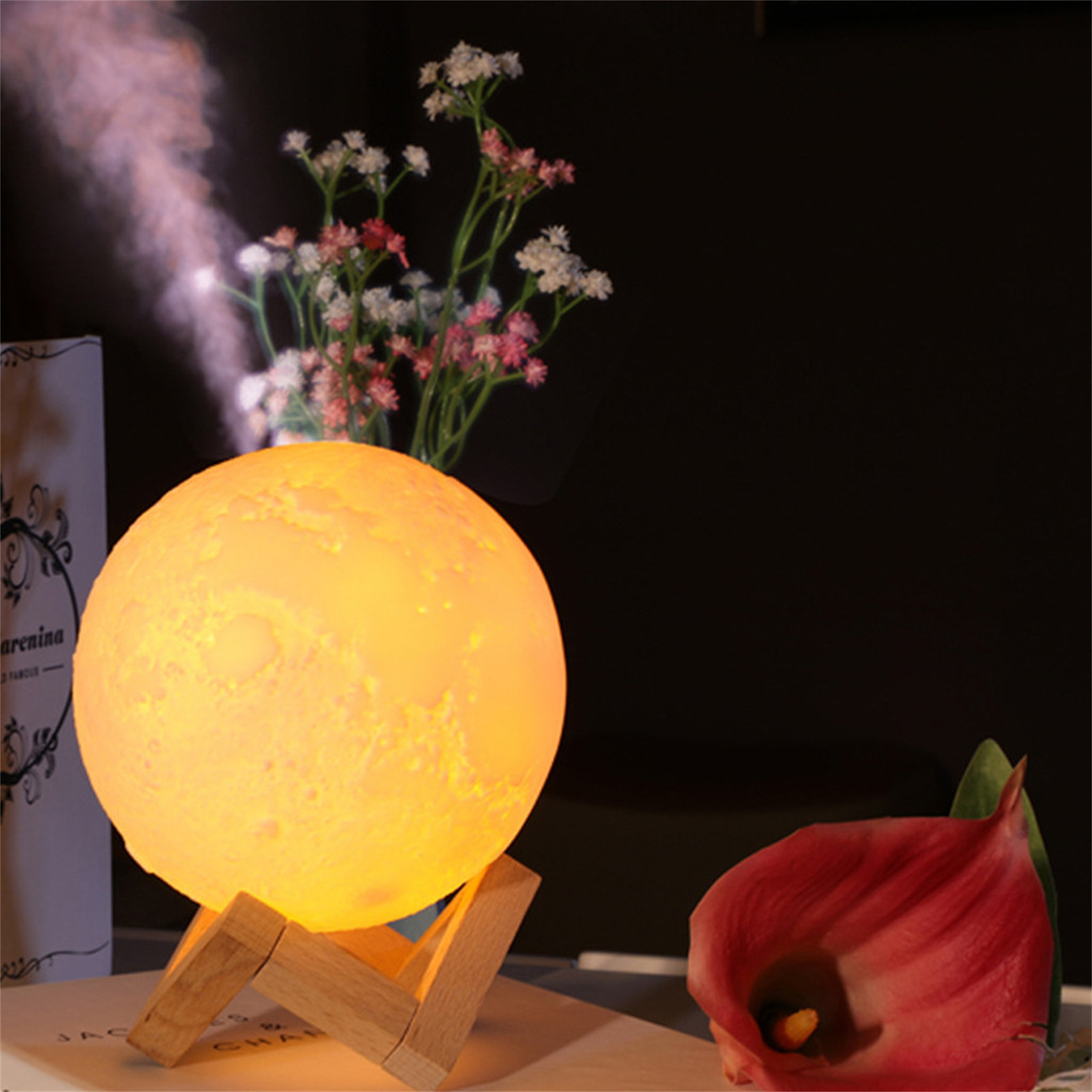 Eine beleuchtete Mondlampe auf einem Holzständer steht in der Nähe von Blumen und wirft sanftes Licht.