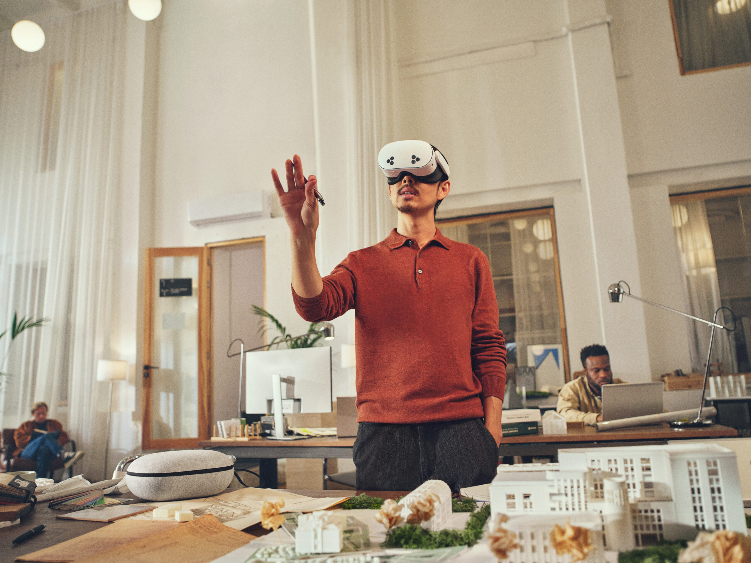 Un uomo con un visore VR interagisce con un modello virtuale. È in un ufficio con modelli e una scrivania.
