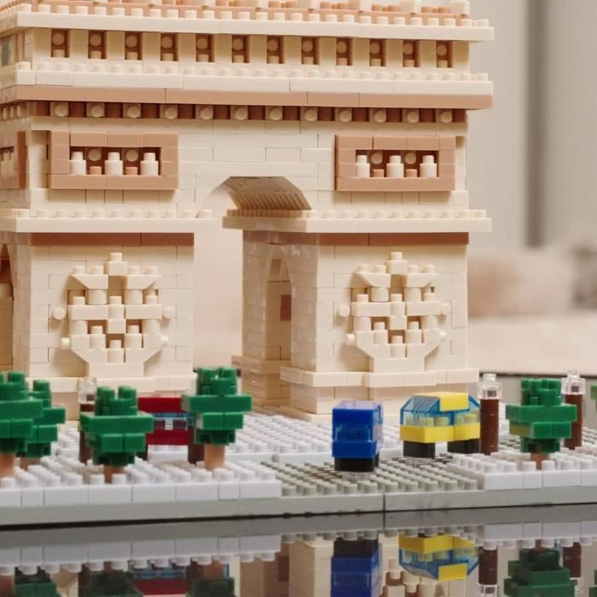 Ein Lego-Modell des Arc de Triomphe. Grüne Bäume und ein blauer Lego-Block im Vordergrund. Hintergrund unscharf.