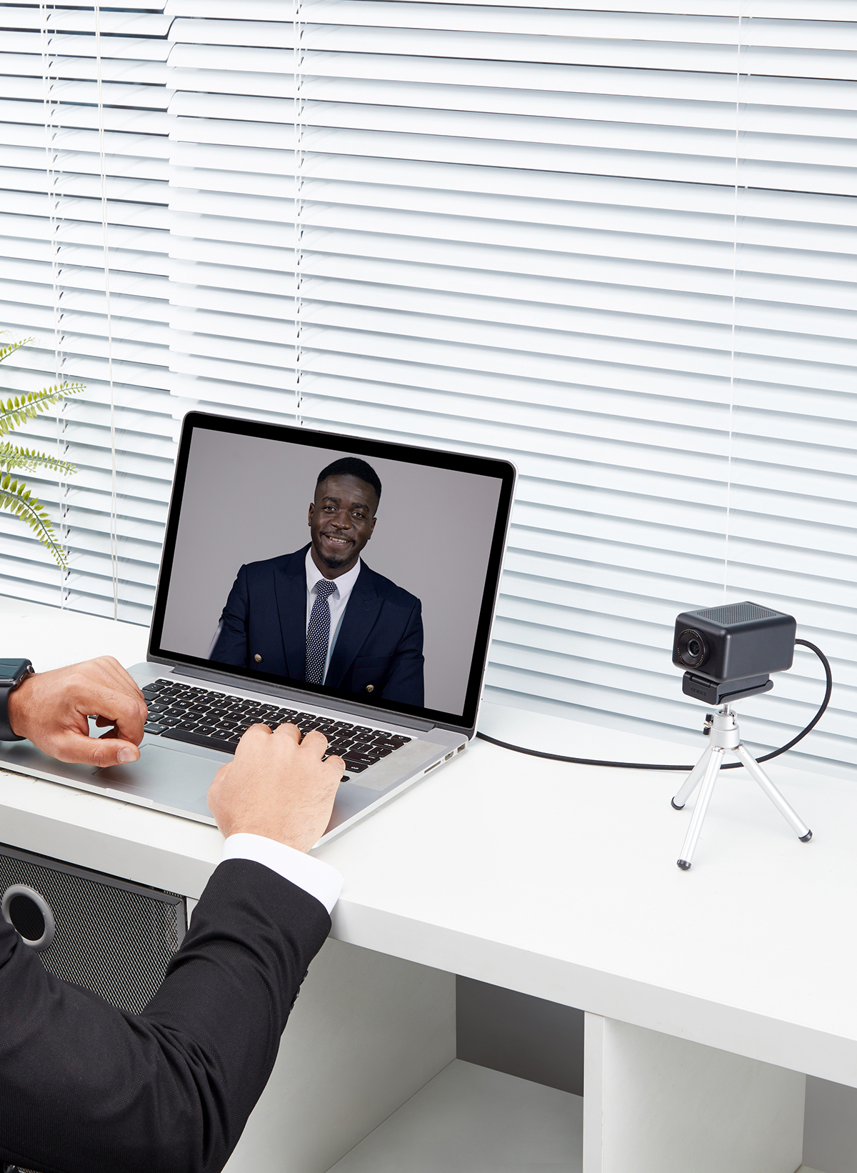 Eine Person, die einen Laptop mit angeschlossener Webcam verwendet. Der Bildschirm zeigt einen Mann im Anzug.
