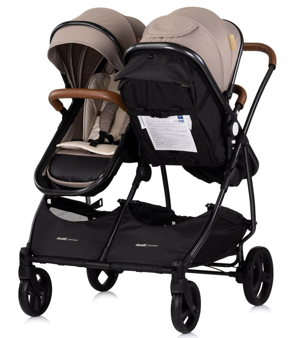 Doppelkinderwagen mit beigefarbenen Verdecken, braunen Griffen, schwarzem Rahmen und schwarzen Körben.