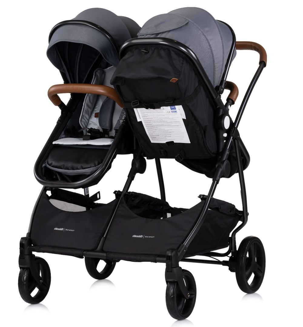 Doppelkinderwagen mit grauen Verdecken, braunen Griffen, schwarzem Rahmen und schwarzen Körben.