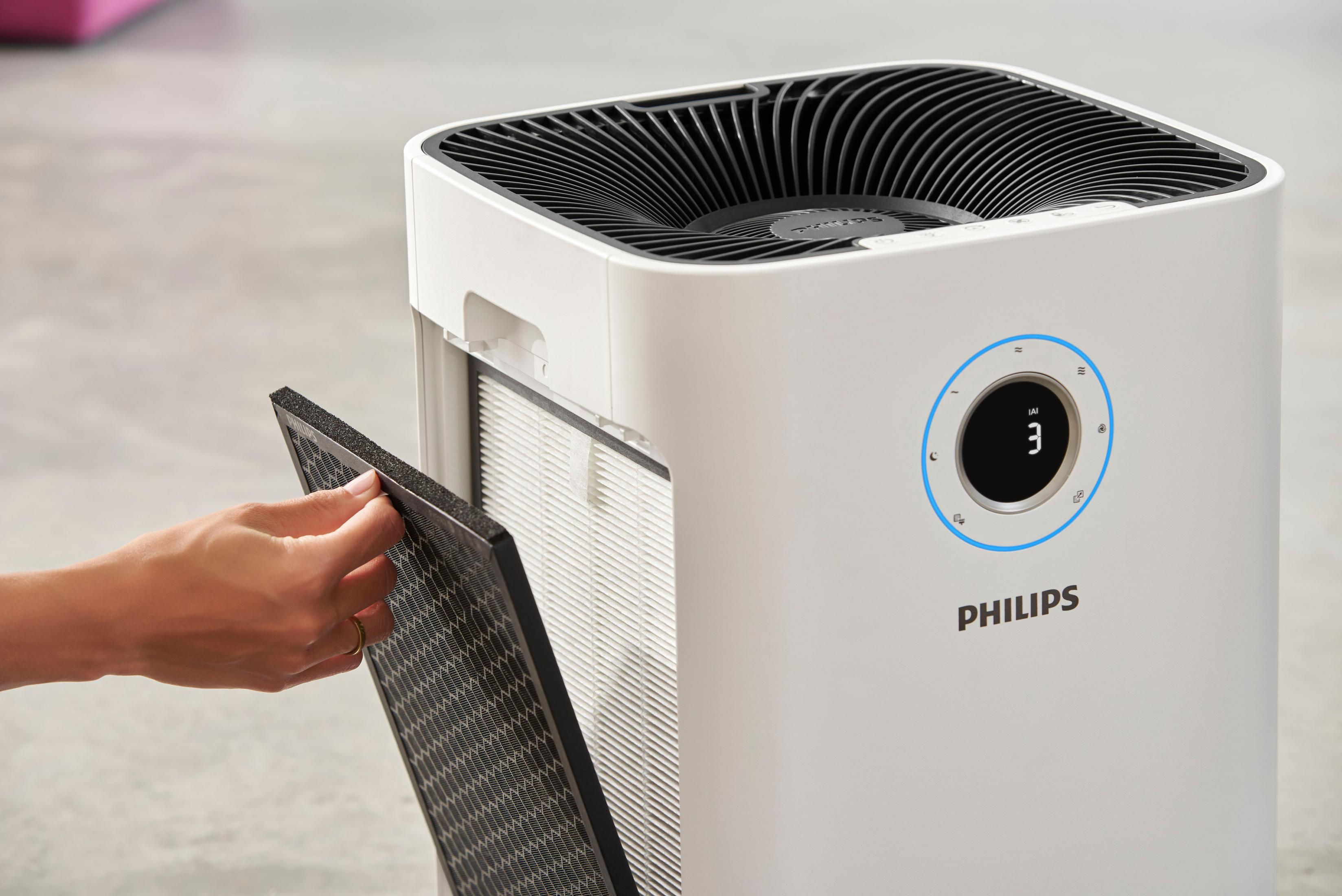 Hand, die einen schwarzen Filter in einen weißen Philips Luftreiniger mit blauem Display einsetzt.
