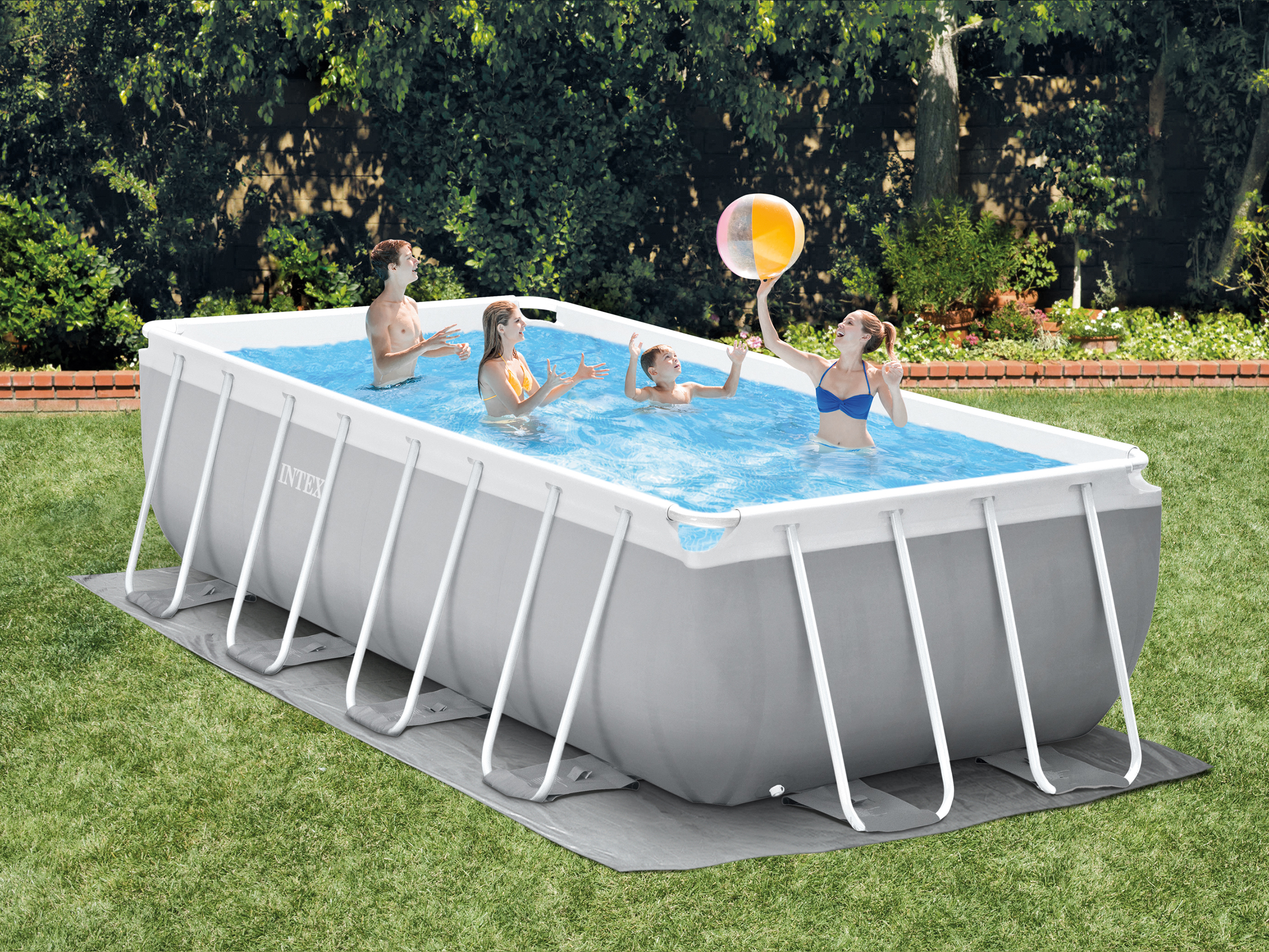 Rodzina korzysta z prostokątnego basenu stelażowego Intex na zielonym podwórku, bawiąc się piłką plażową.