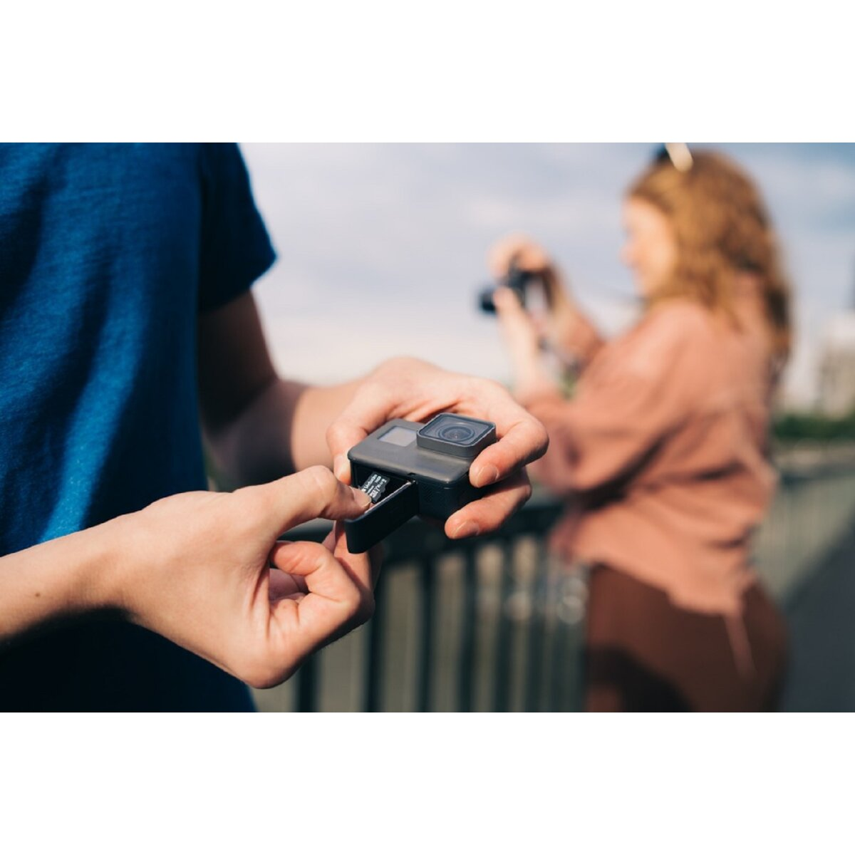 Osoba wkładająca baterię do kamery GoPro, druga osoba w tle.