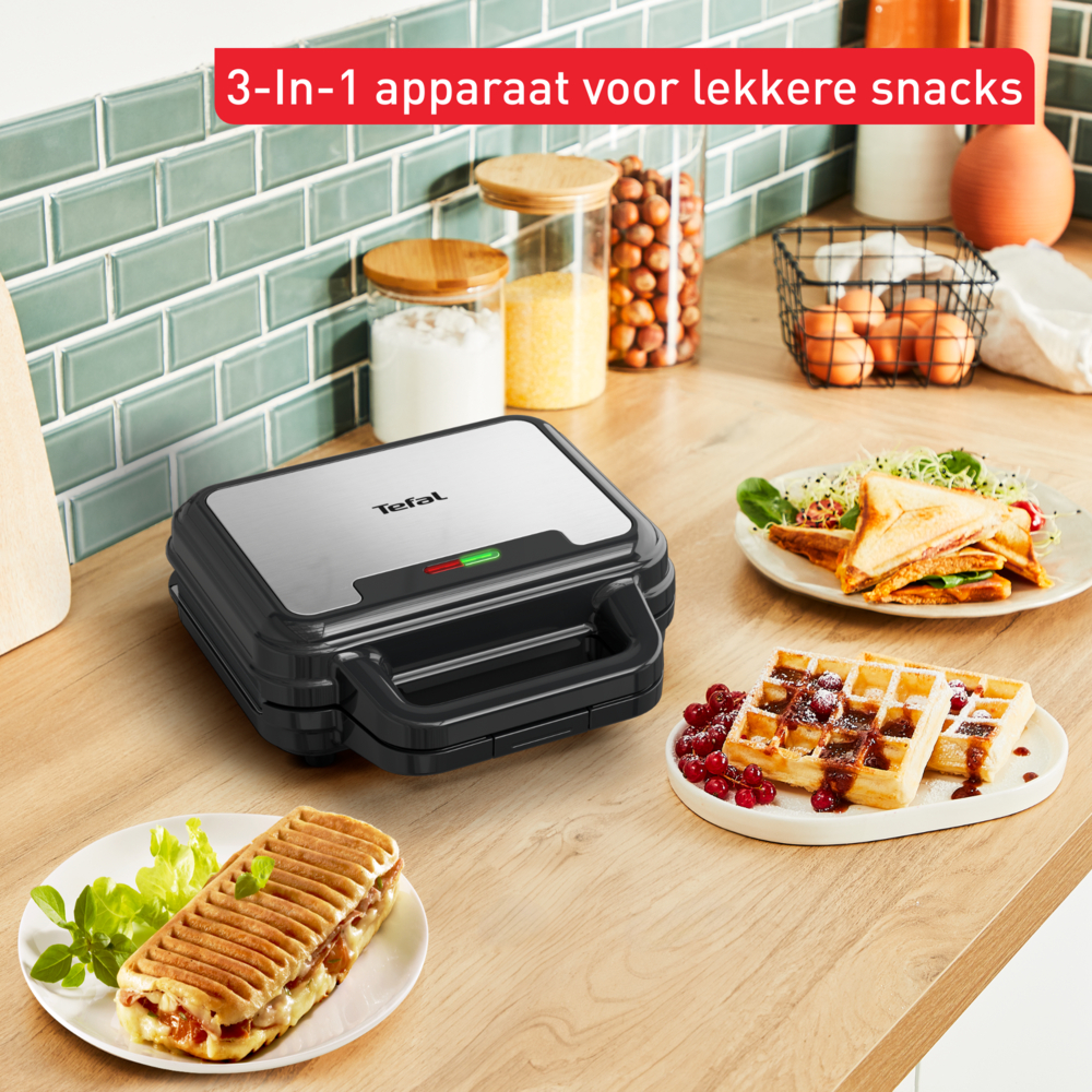 Black Tefal waffle maker with waffles, sandwiches and a panini on a wooden counter.