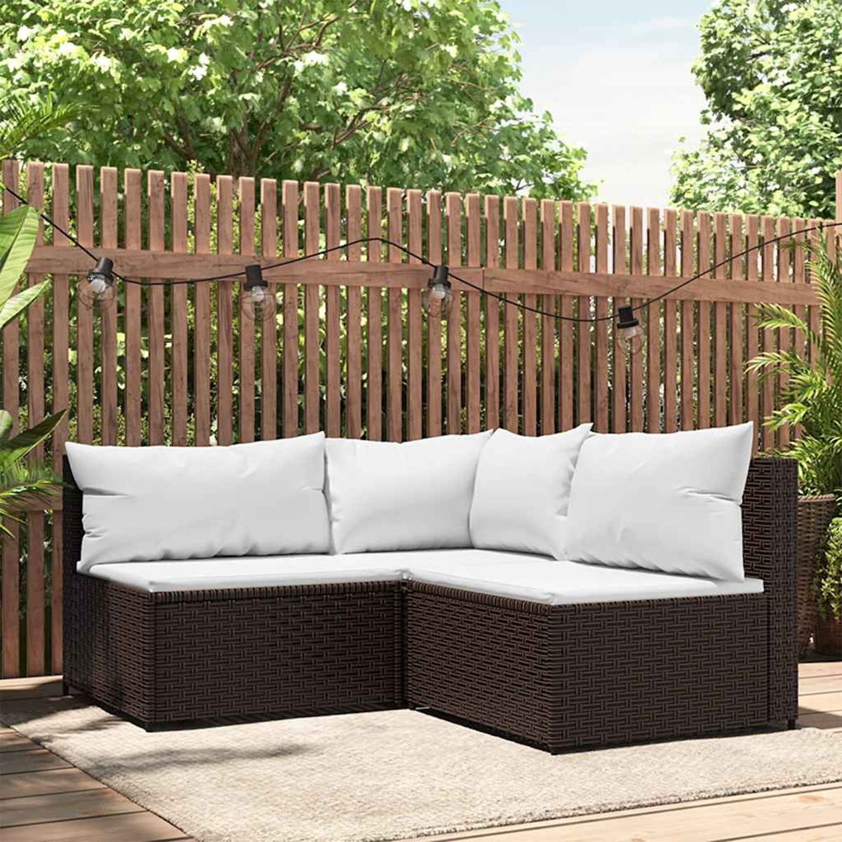 Braunes Ecksofa aus Korbgeflecht, weiße Kissen. Outdoor-Setting mit Holzzaun im Hintergrund.