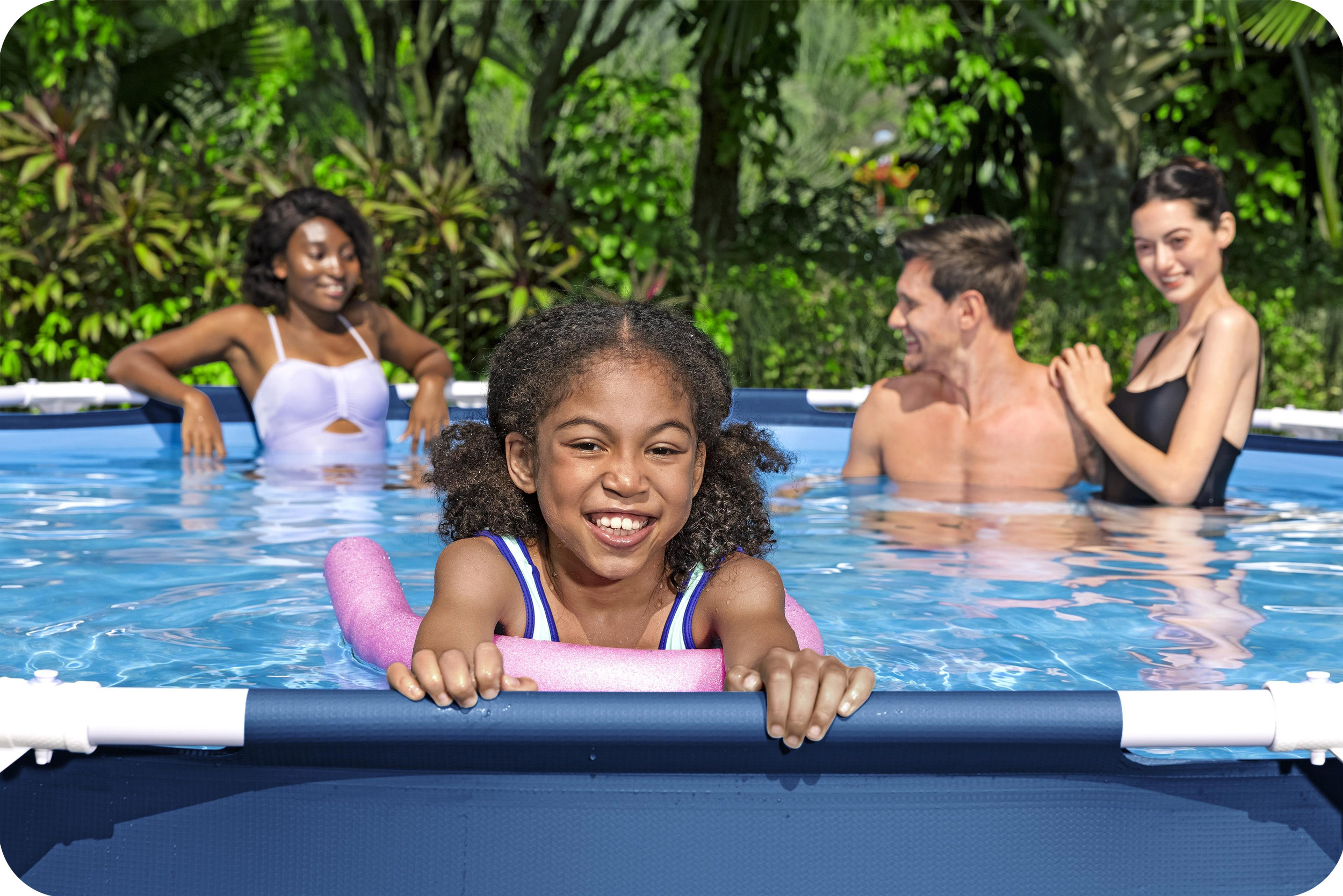 Dziewczyna w basenie z makaronem. Trzy osoby w tle w basenie, otoczone zielenią.