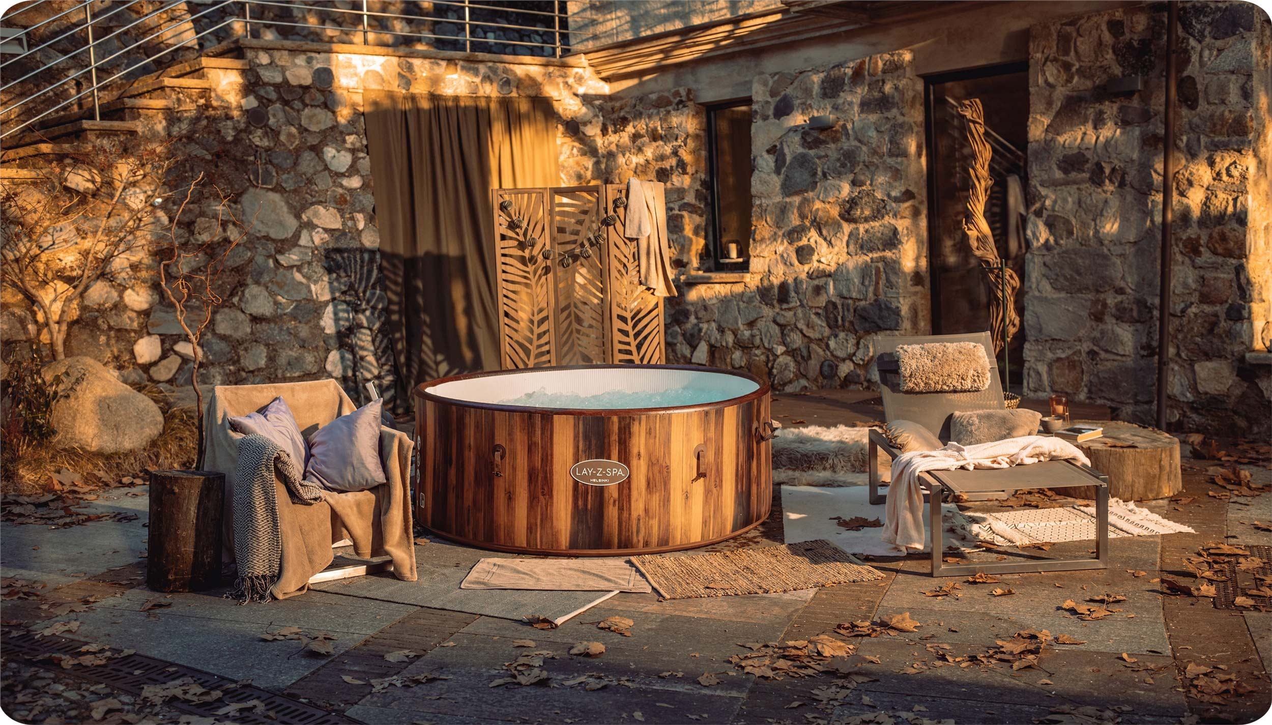 Drewniane spa w plenerze, z meblami i elementami dekoracyjnymi wokół niego, o zachodzie słońca.