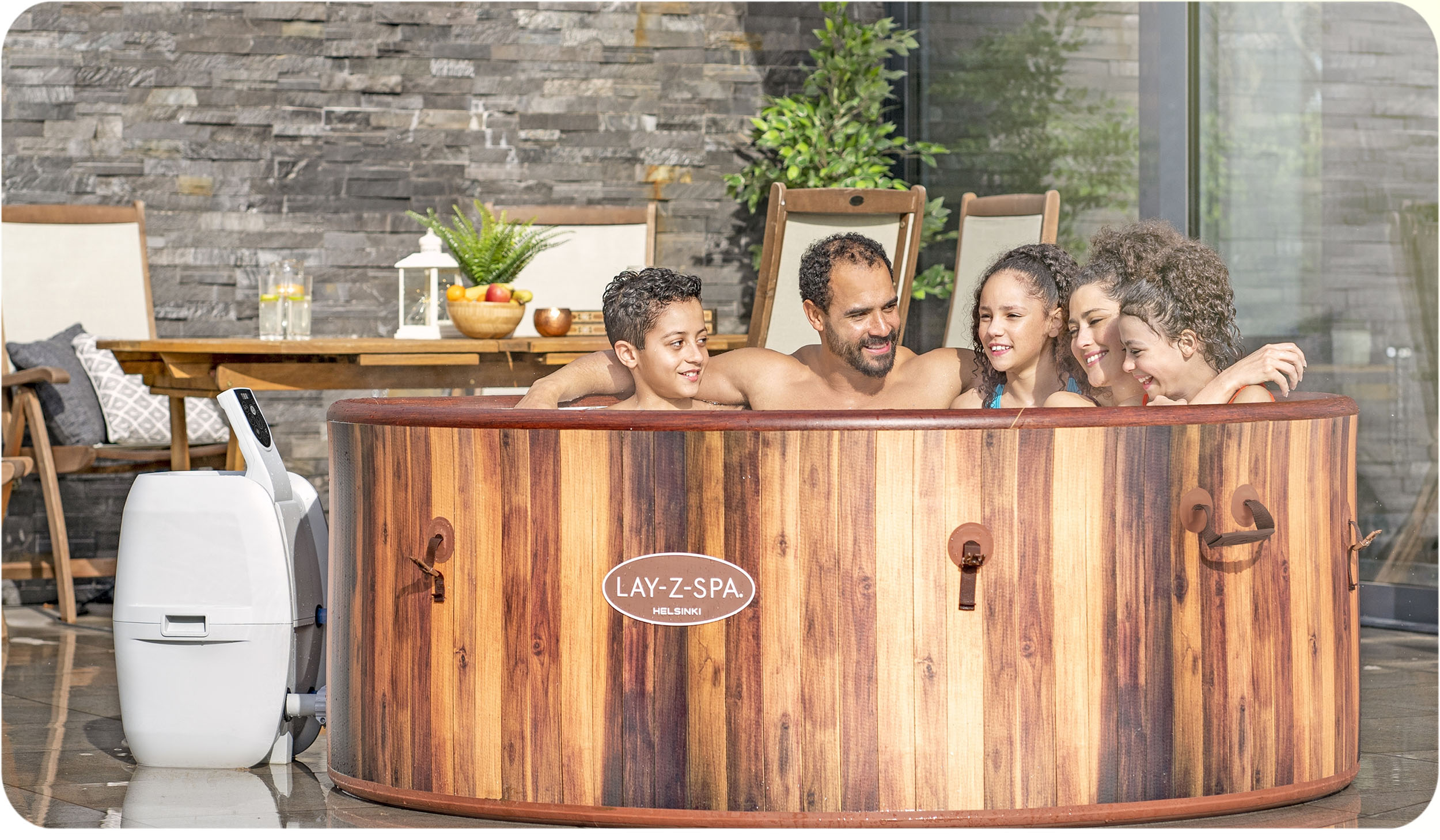 Rodzina w wannie z hydromasażem Lay-Z-Spa Helsinki, z drewnianym wykończeniem, na zewnątrz, uśmiechnięta i śmiejąca się.