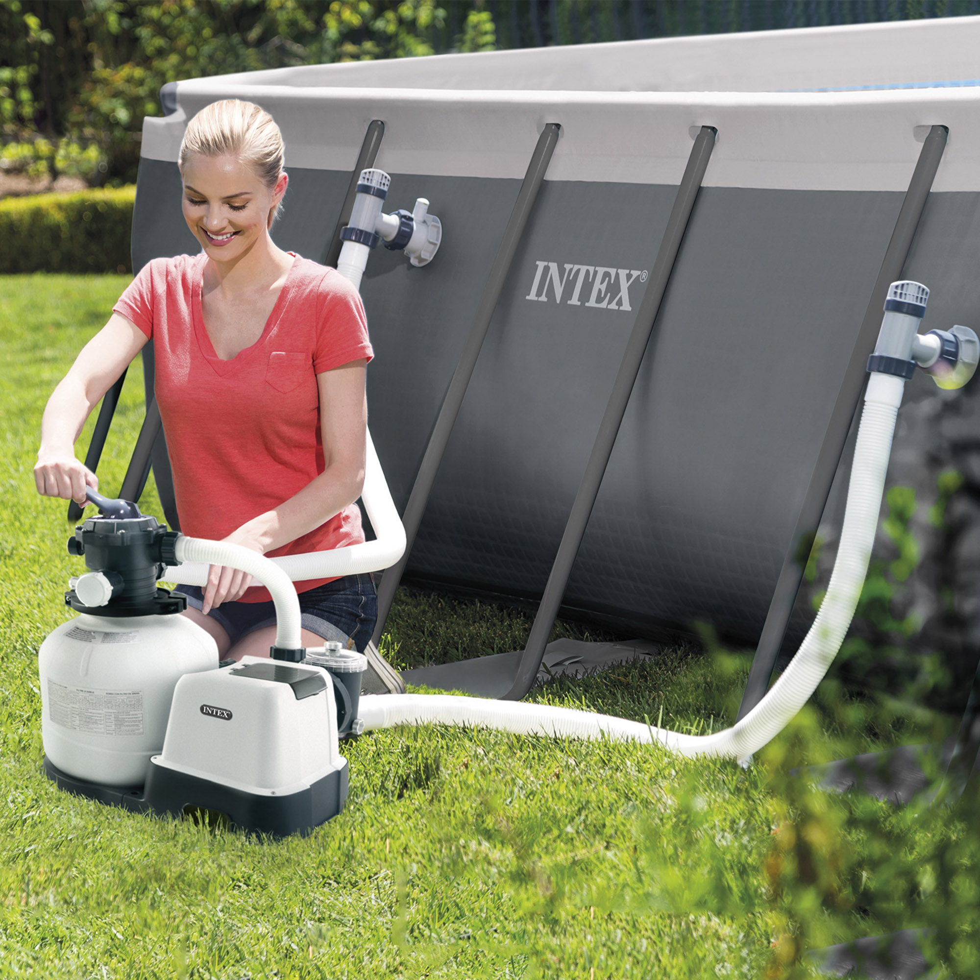 Kobieta używa pompy do filtrowania basenu. Uśmiecha się i klęczy na trawie.