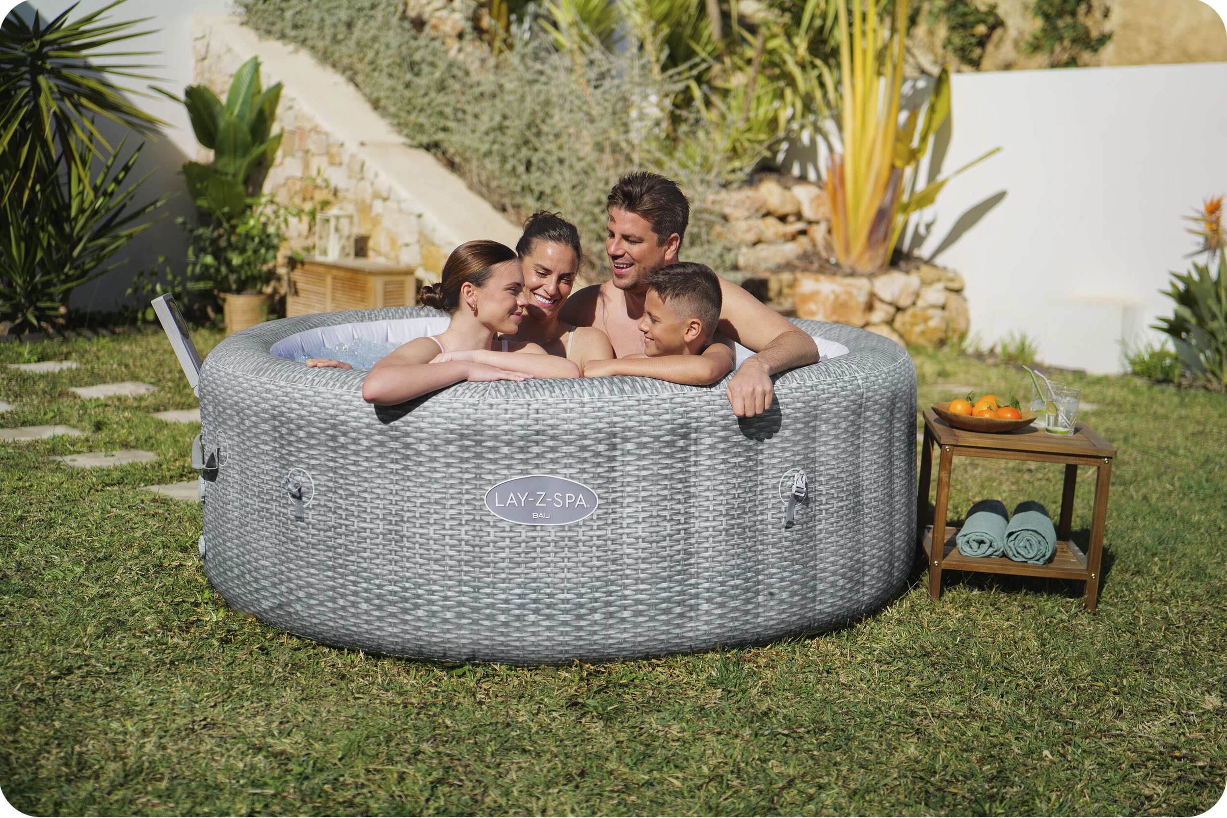 Rodzina w szarej wannie z hydromasażem na trawie. Wanna ma tkany wzór.