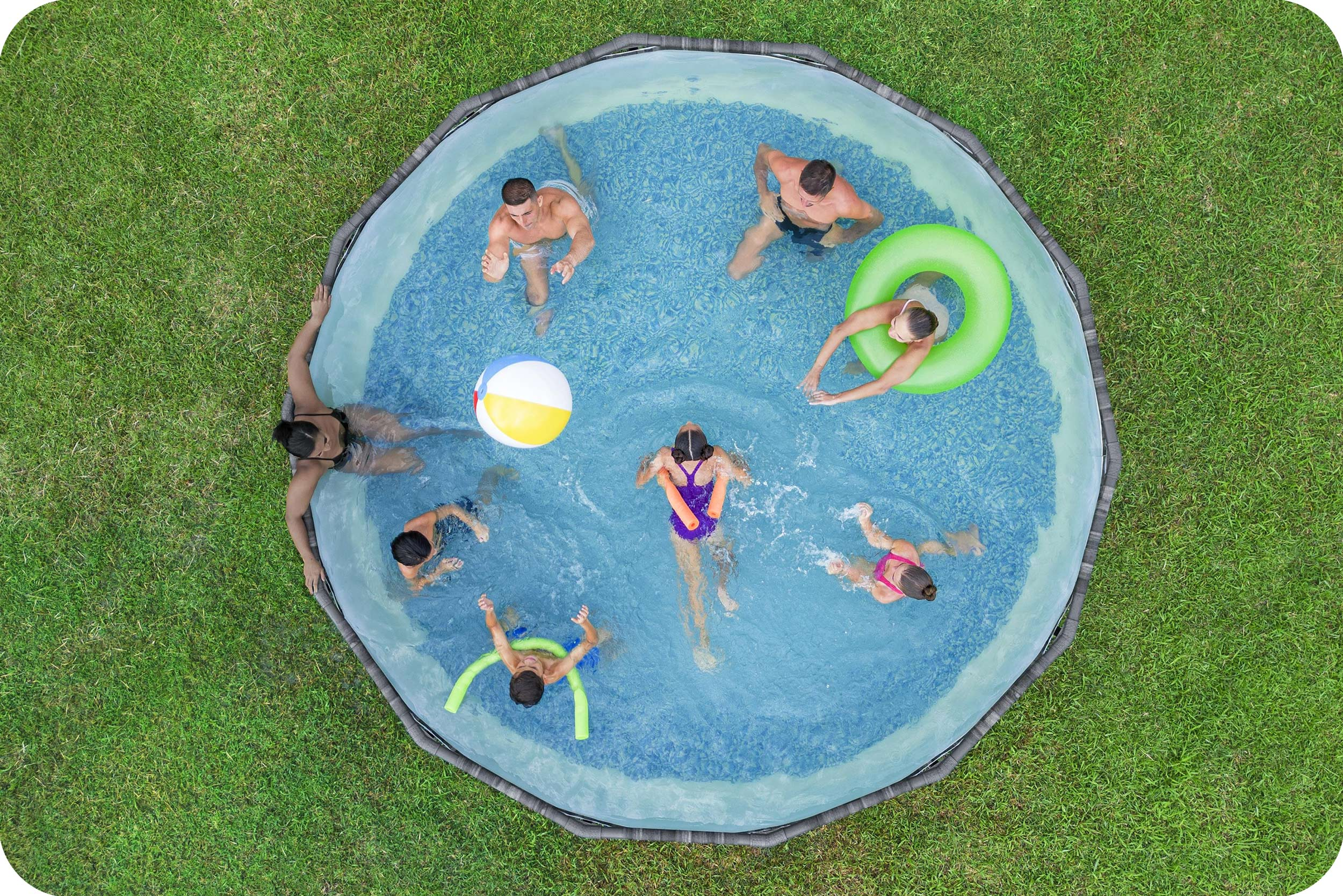 Widok z góry na okrągły basen z pływającymi ludźmi. Zielona trawa otacza basen. Ludzie cieszą się wodą.