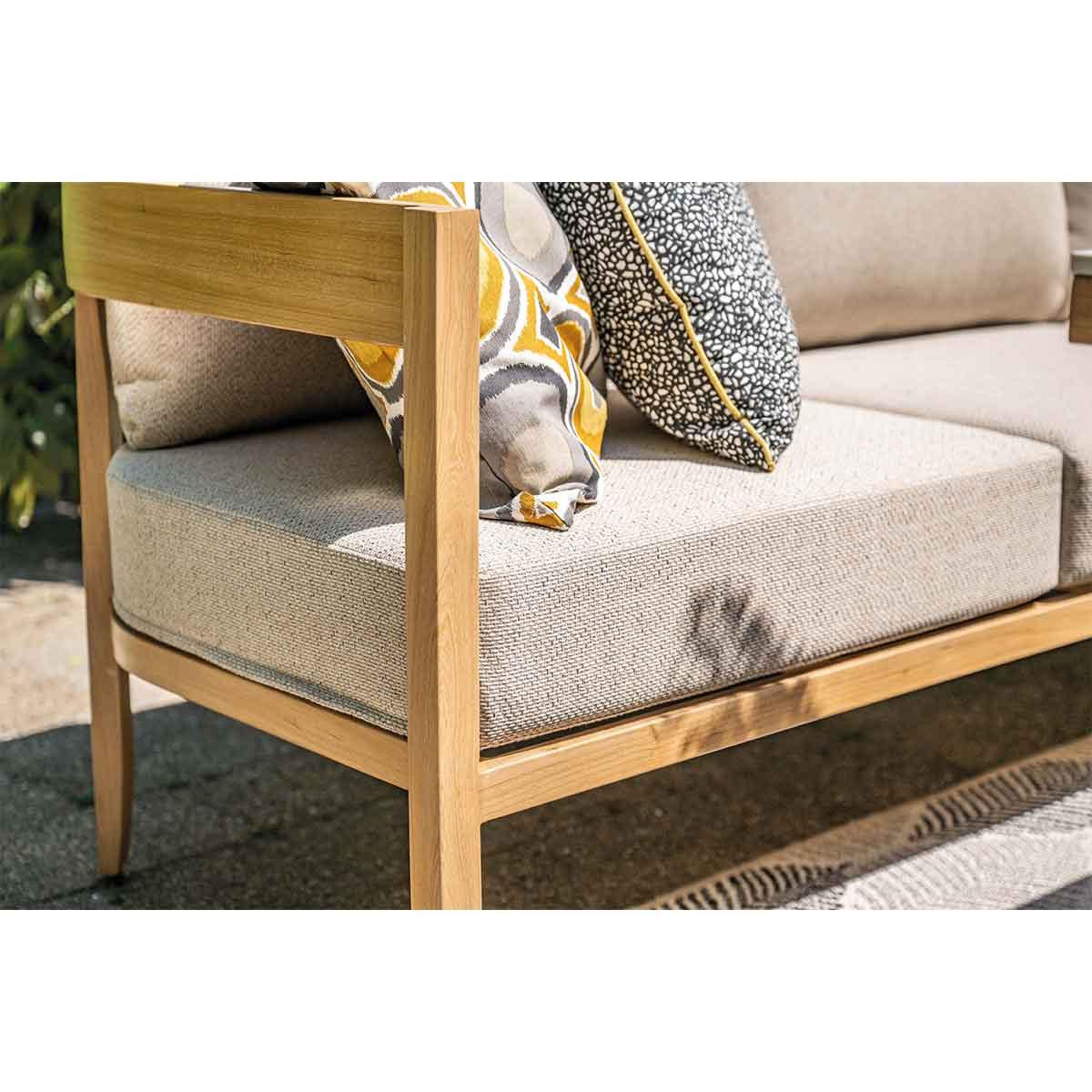 Een bank met licht houten frame, beige kussens en kleurrijke sierkussens.