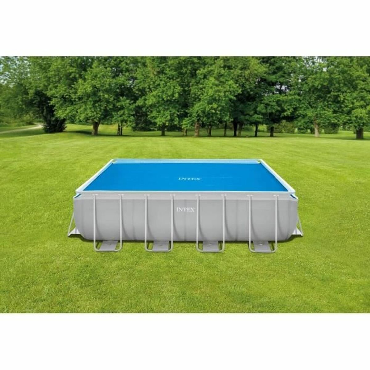 Ein rechteckiger Pool mit blauer Abdeckung, umgeben von grünem Gras und B äumen.