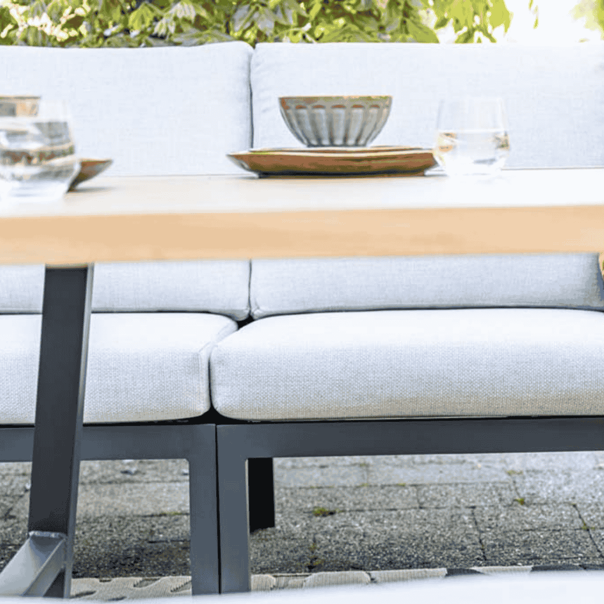 Gros plan sur mobilier extérieur. Coussins gris clair, table en bois avec nourriture et boissons.