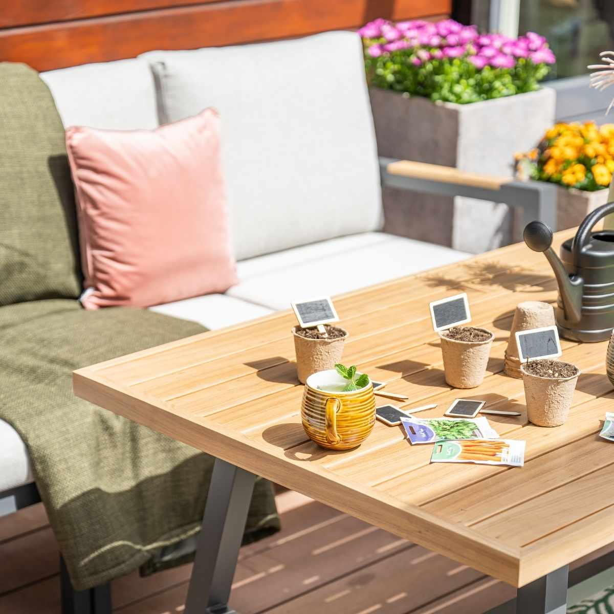 Tafel met planten, koffiekopje en zaden. Buitenscène met bank, kussens en planten. Close-up.