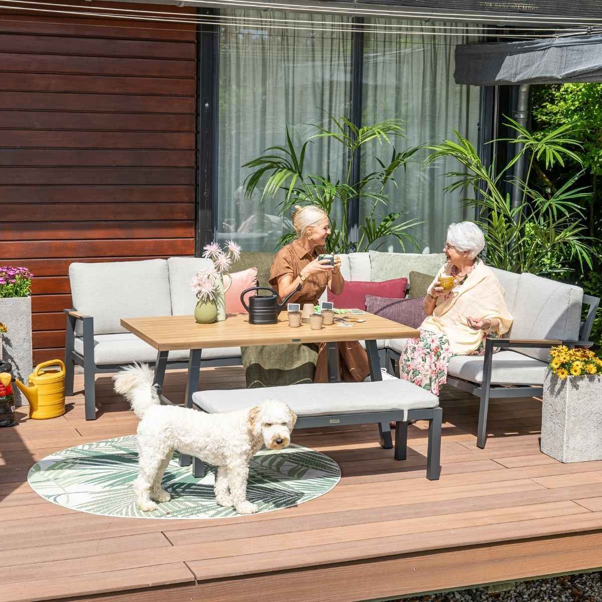 Twee vrouwen zitten aan een buitentafel, met een hond. Outdoor meubelopstelling.