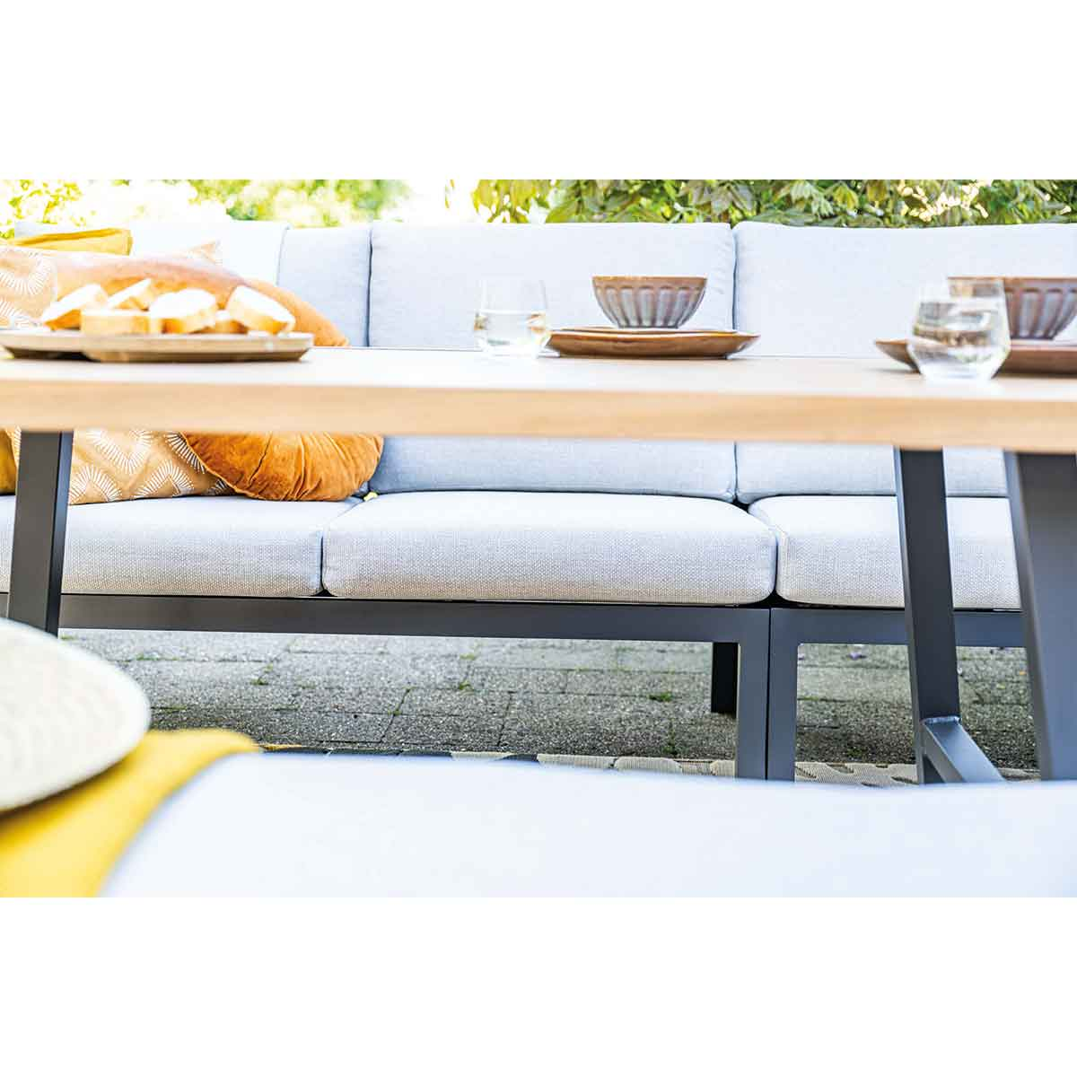 Gros plan sur mobilier extérieur. Coussins gris clair, table en bois avec nourriture et verres.