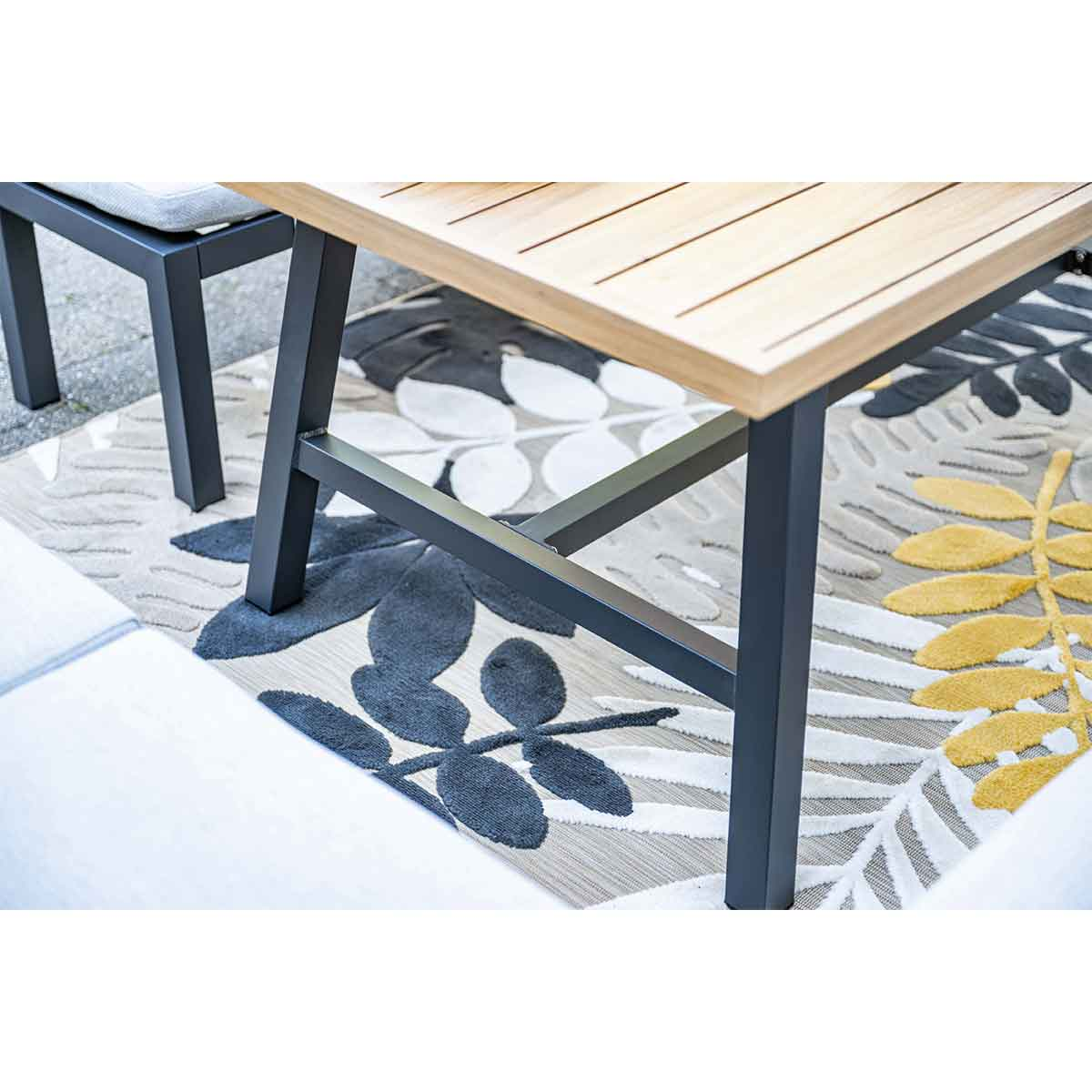 Gros plan sur les pieds d'une table en bois et un banc. Le tapis a un motif de feuilles.