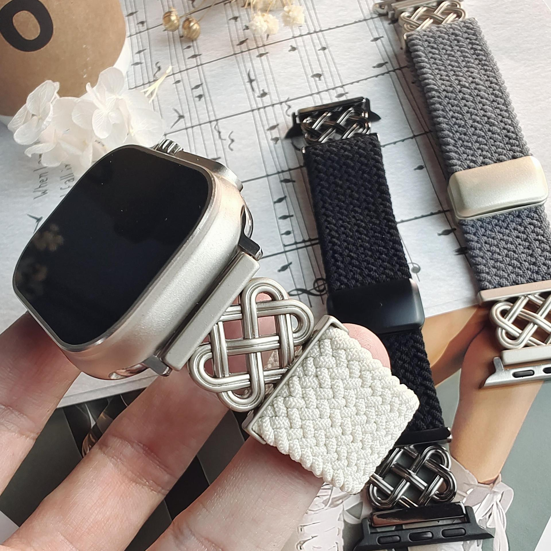 Eine Hand, die eine Smartwatch und drei Uhrenarmbänder hält. Die Armbänder sind weiß, schwarz und grau. Weißer Hintergrund.