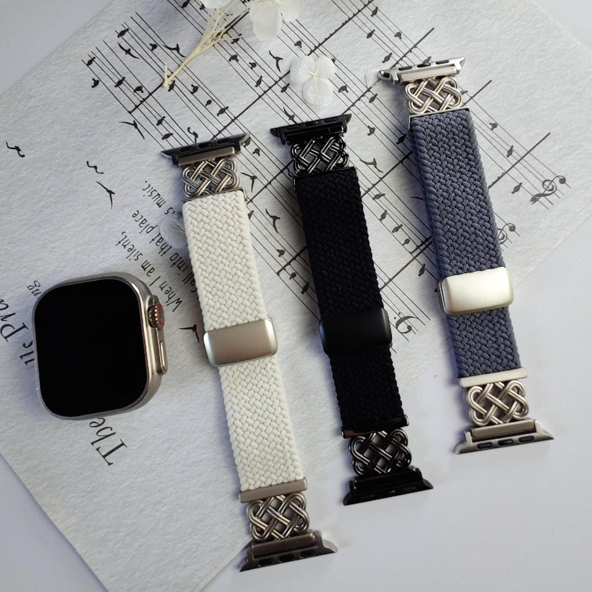 Drei Uhrenarmbänder: weiß, schwarz und grau, mit silbernen Verschlüssen, auf Noten angeordnet. Eine Uhr links.