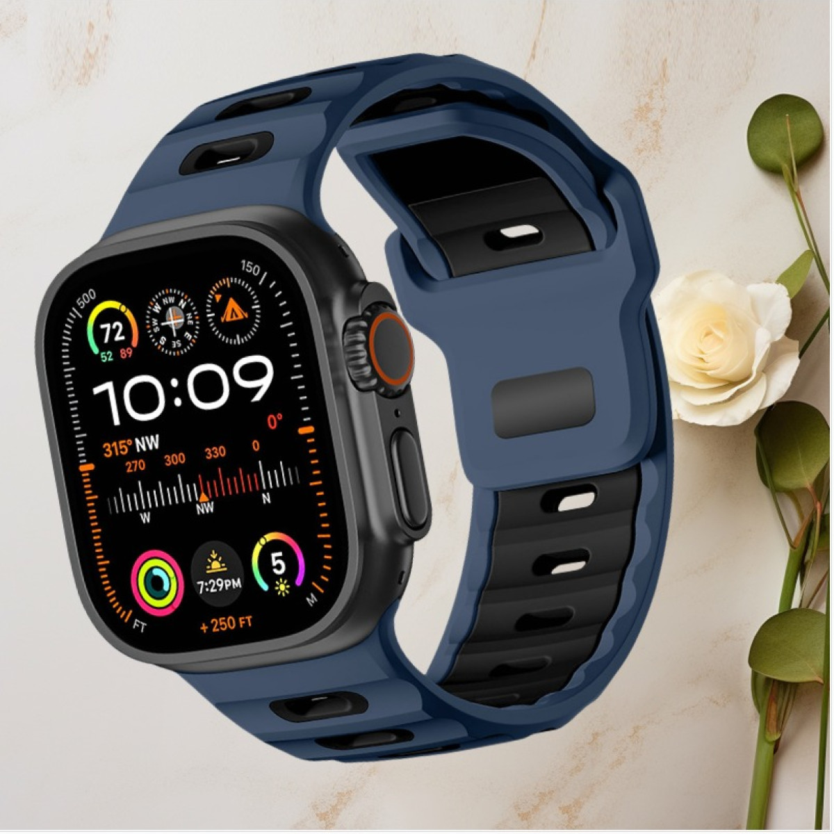 Smartwatch con cinturino blu. Lo schermo mostra vari dati. Fiore bianco e superficie color crema sullo sfondo.
