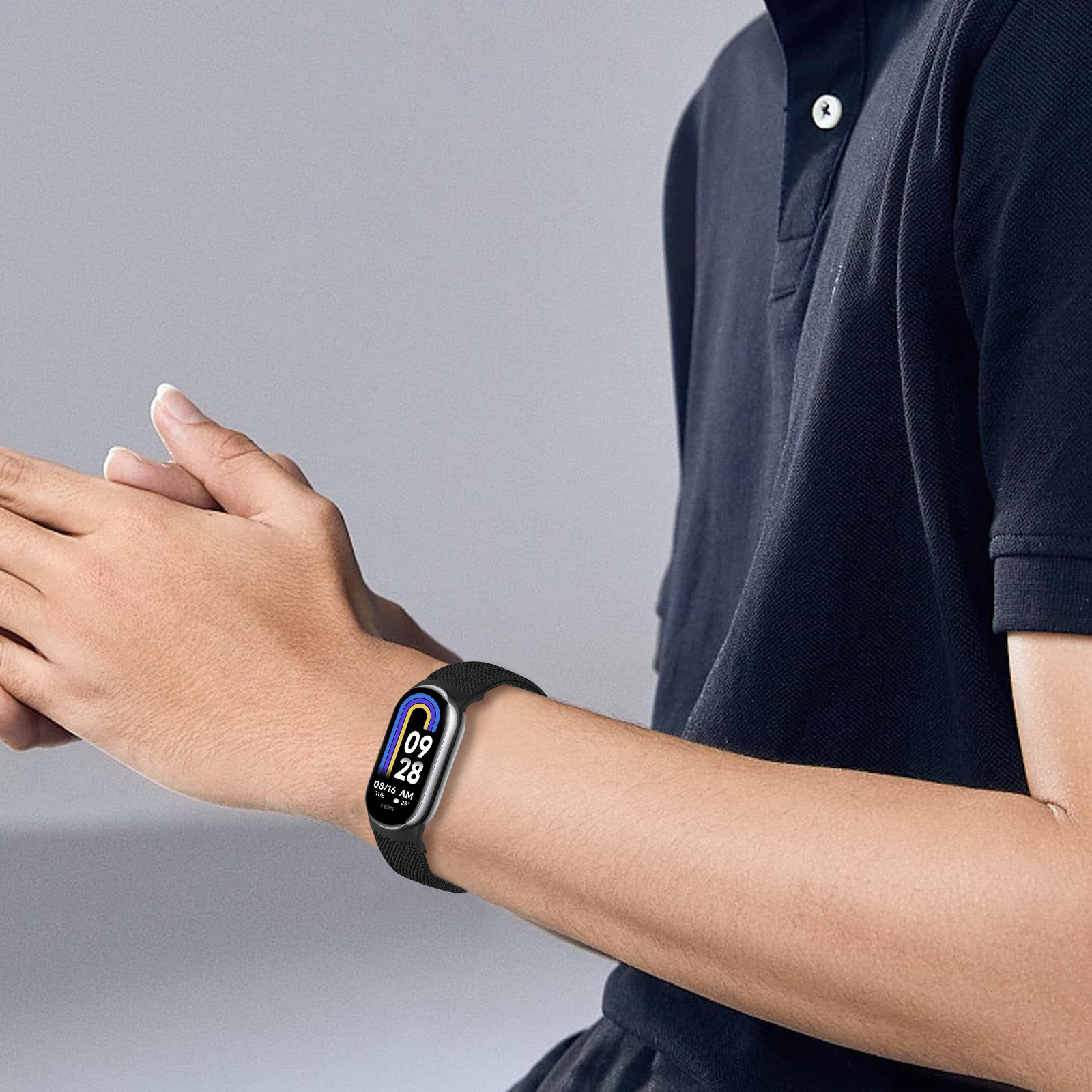 Eine Person trägt eine schwarze Smartwatch mit schwarzem Armband am Handgelenk. Die Uhr zeigt Datum und Uhrzeit an.