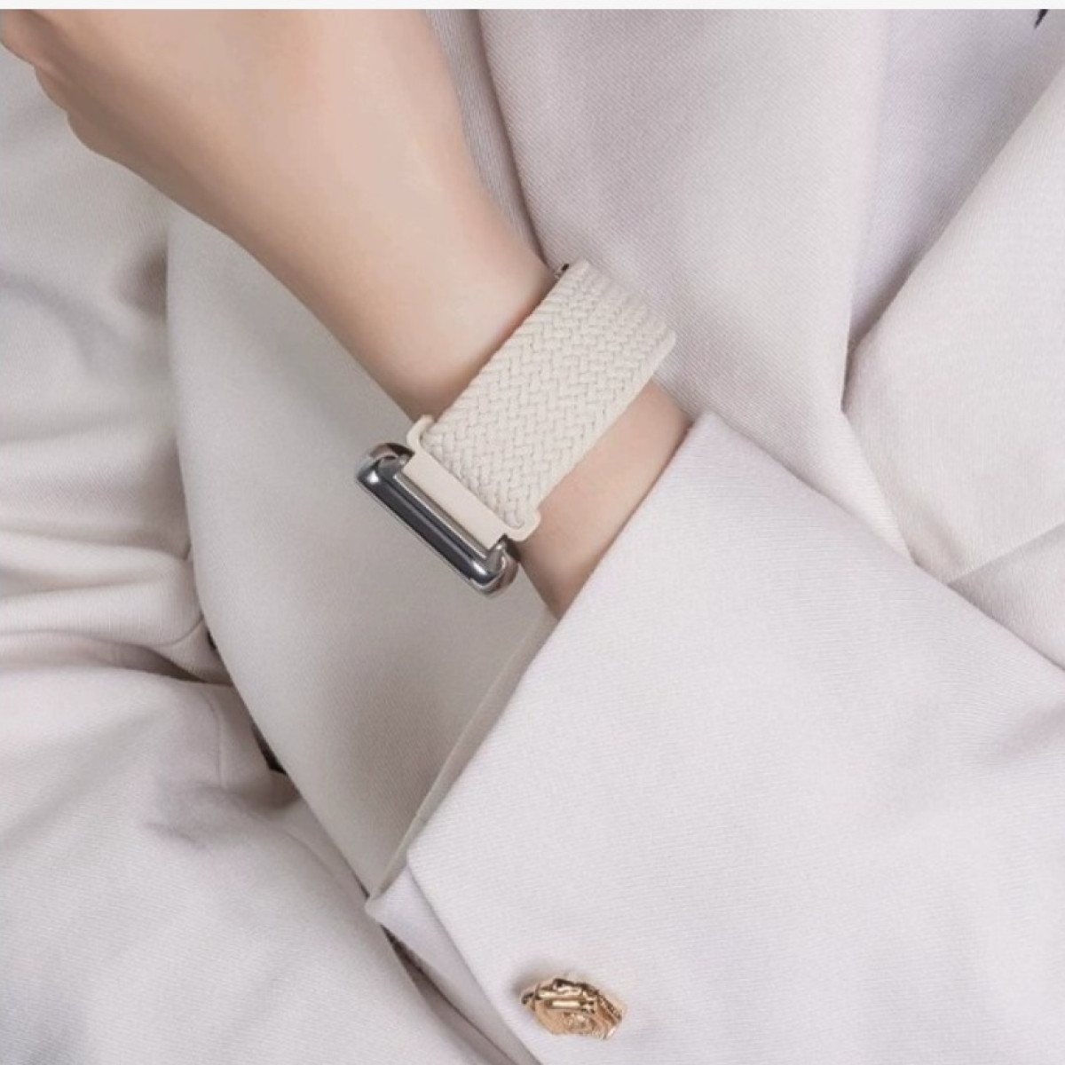 Handgelenk mit Uhr, trägt einen weißen Blazer mit goldenem Knopf.